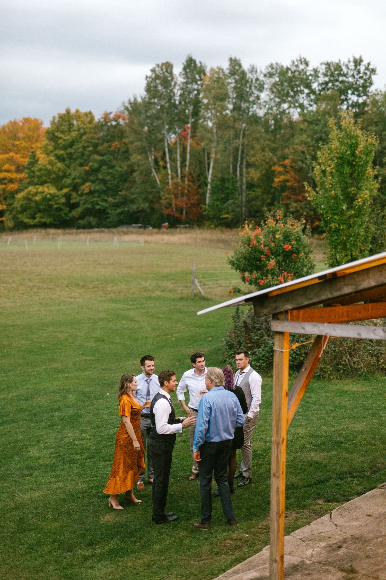 Small group gathers on autumn lawn with colorful fall foliage in background during outdoor event.