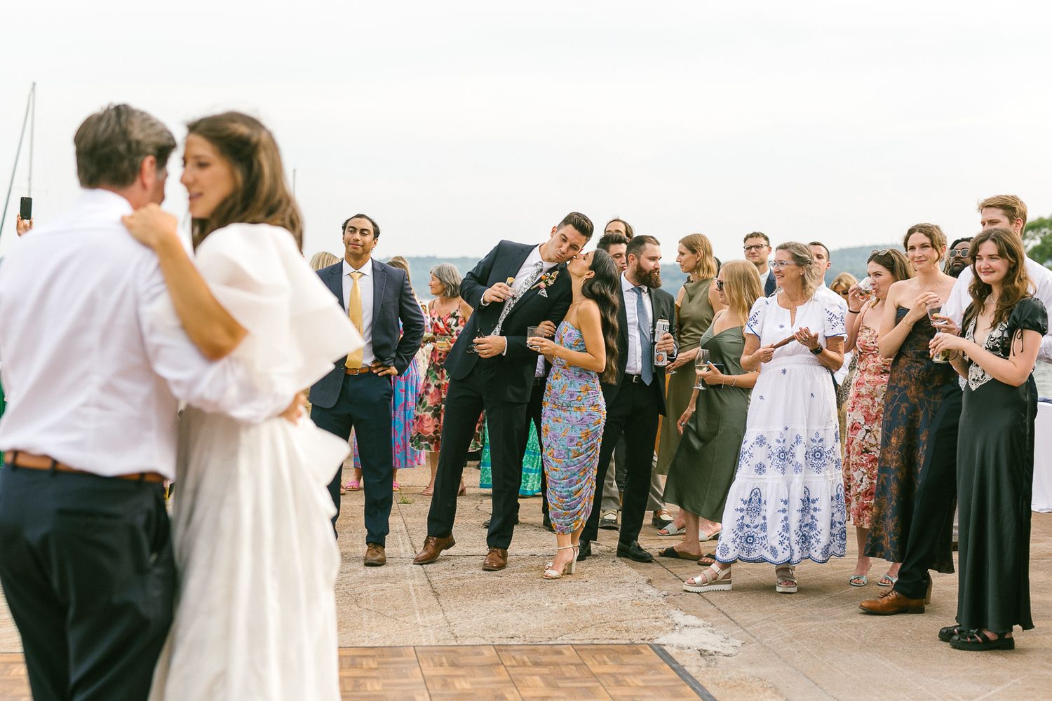 Wedding party and guests gather on beach for celebration photos.
