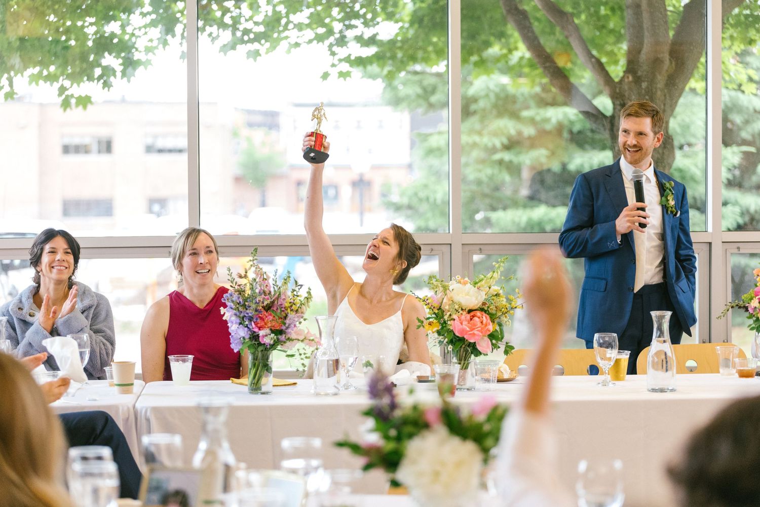 Wedding reception scene with guests raising glasses during toasts at tables decorated with floral centerpieces.