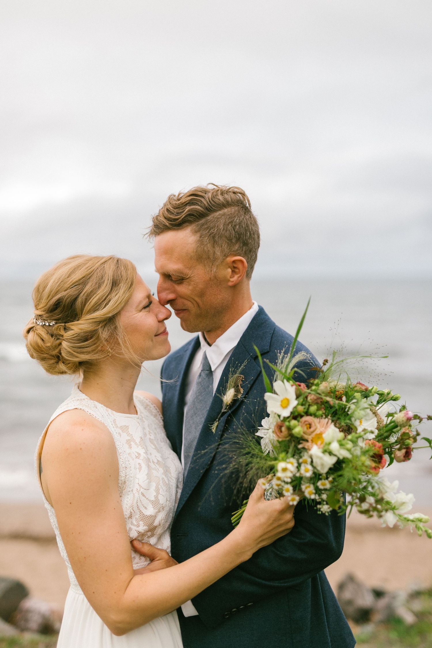 An intimate wedding moment captured on a cloudy beach with white and green floral bouquet.