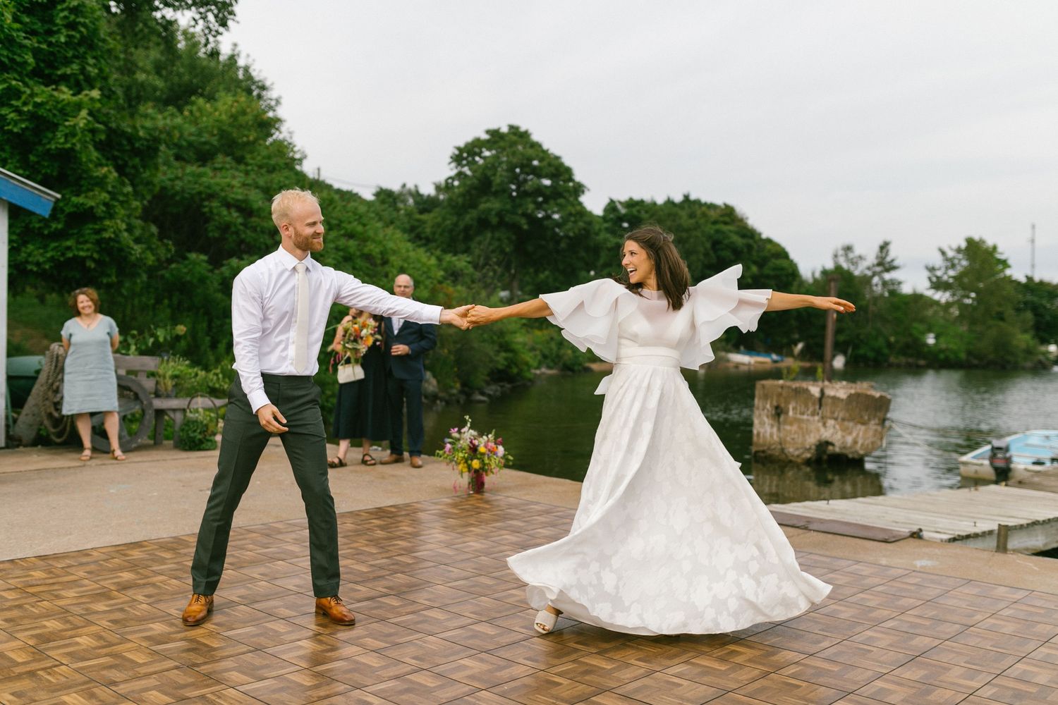Wedding party members dance and twirl on an outdoor patio during a festive celebration.