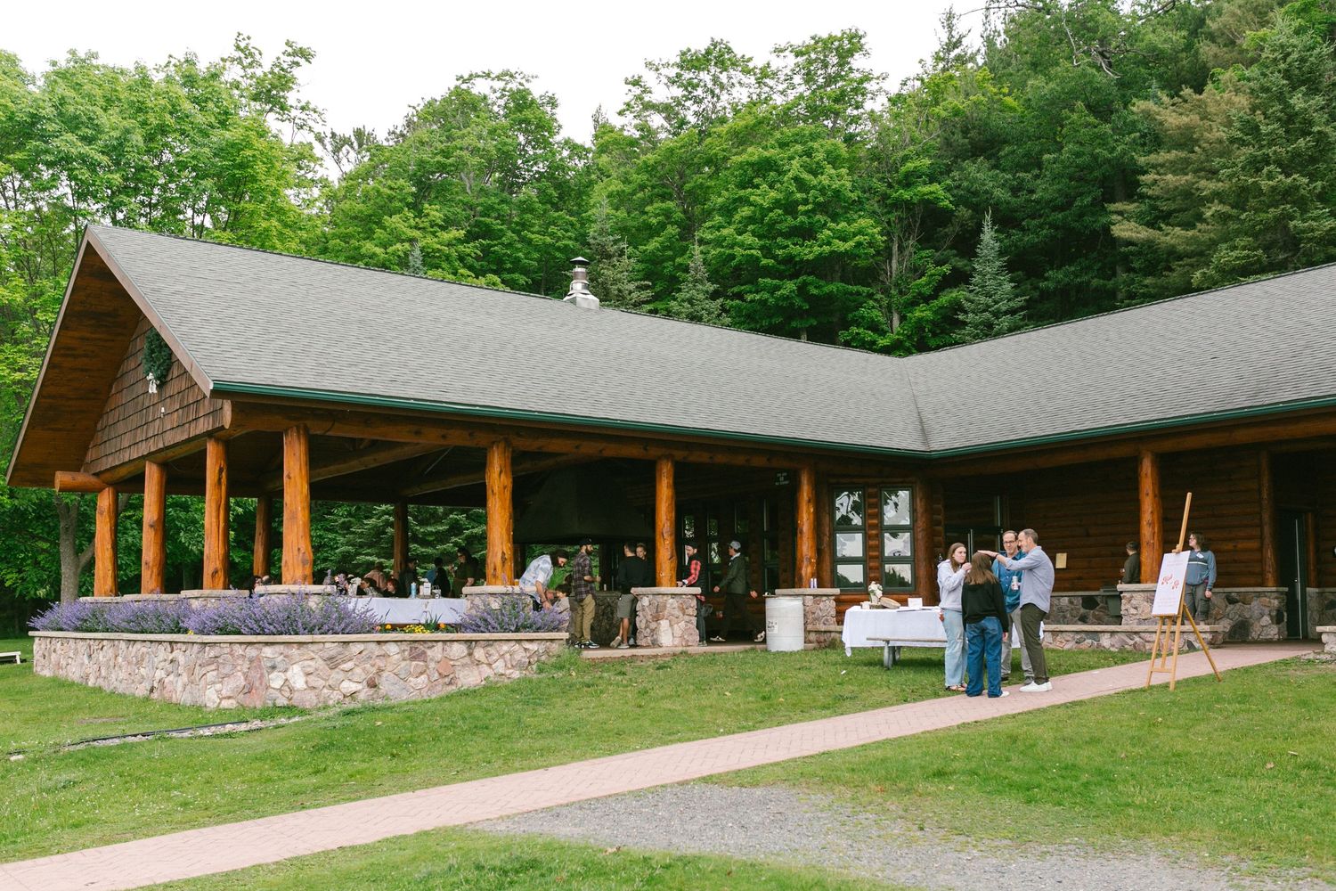 A modern lodge building with stone walls and wooden beams stretches across a green hillside surrounded by trees.