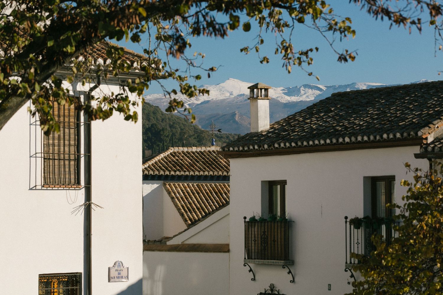 White Spanish colonial buildings with terracotta roofs and wrought iron balconies against a mountainous backdrop.
