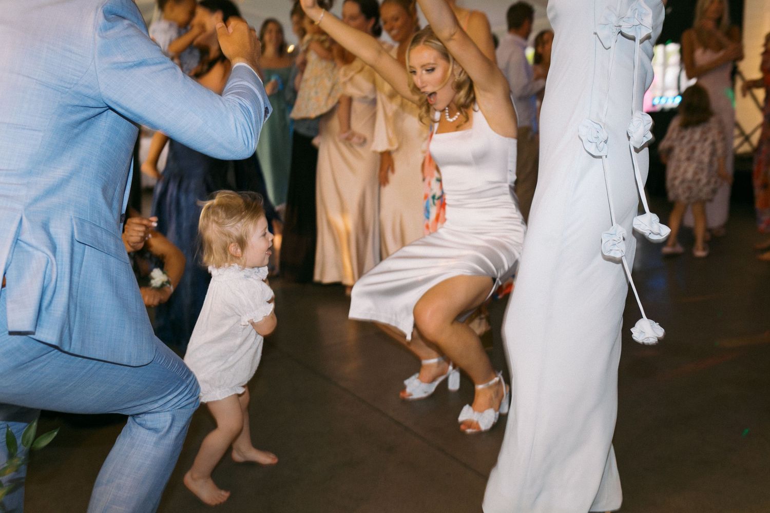 Wedding guests in formal attire dancing together at an indoor reception.