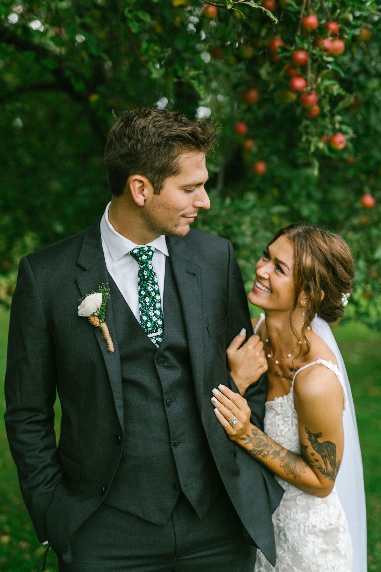 A couple in wedding attire share a tender moment in an apple orchard on their special day.
