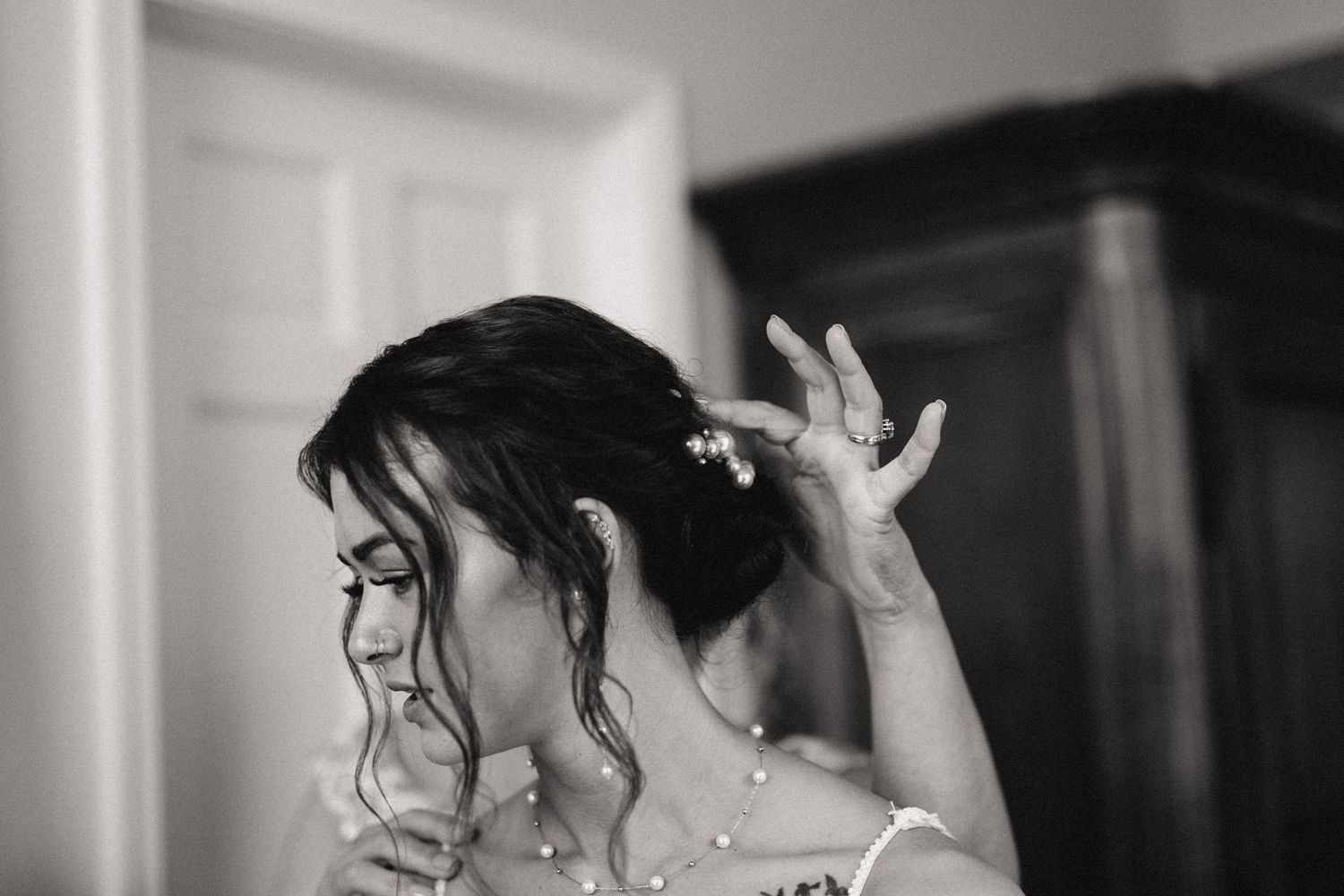 A bride in black and white adjusts her hair while getting ready for her wedding ceremony.