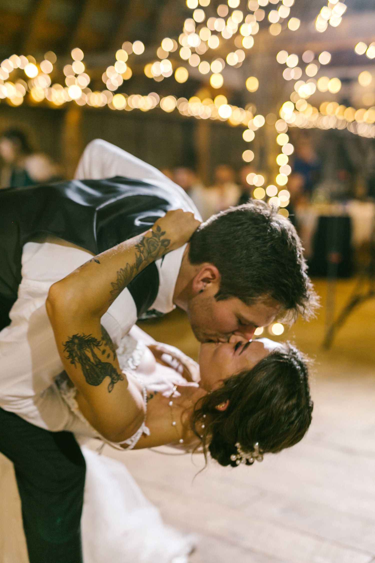 Romantic couple sharing an intimate kiss under twinkling string lights at an evening celebration.
