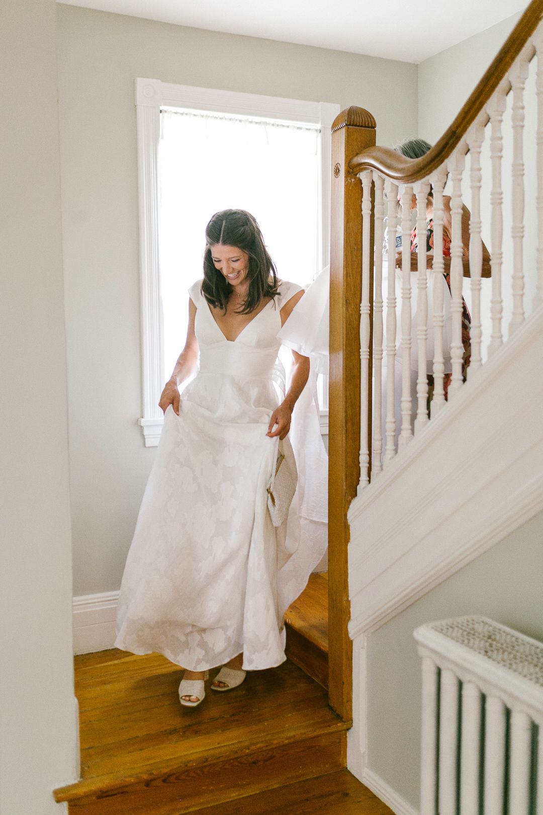 A flowing white wedding dress descends a wooden staircase with natural light streaming in.