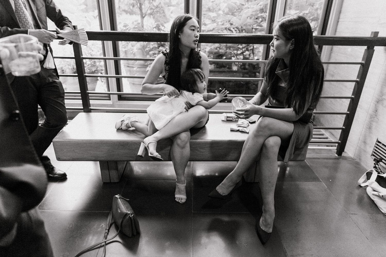 Two women in black and white photo sitting on bench chatting at wedding reception.