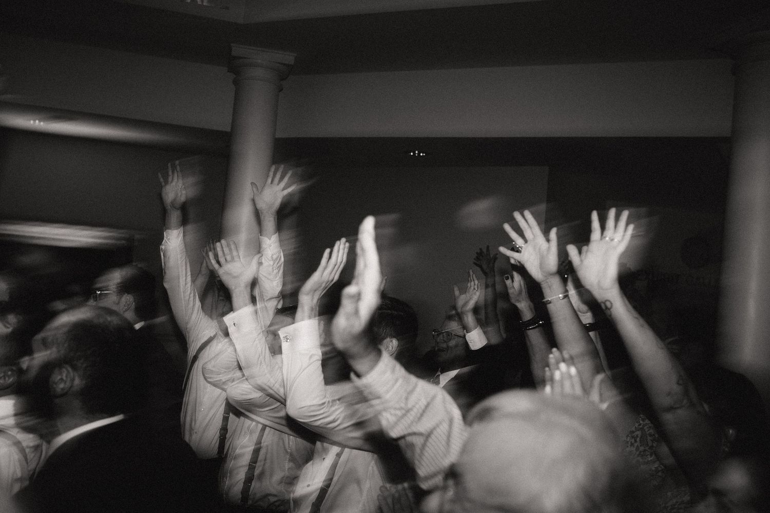 A black and white photo showing raised hands and arms of people in a crowd.