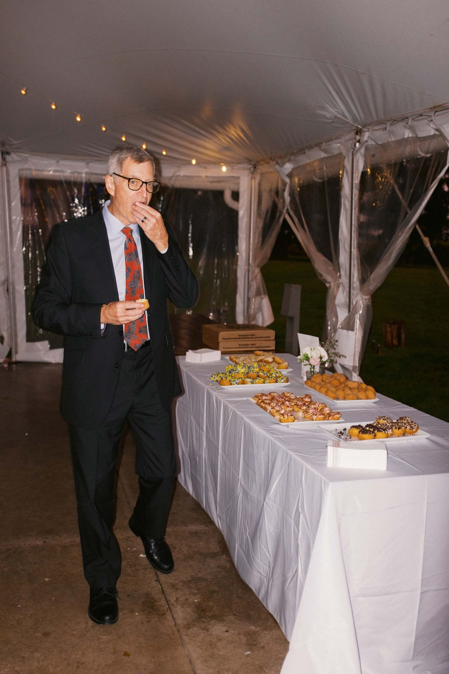 A buffet table with white linens is set up under an outdoor tent at an evening event.