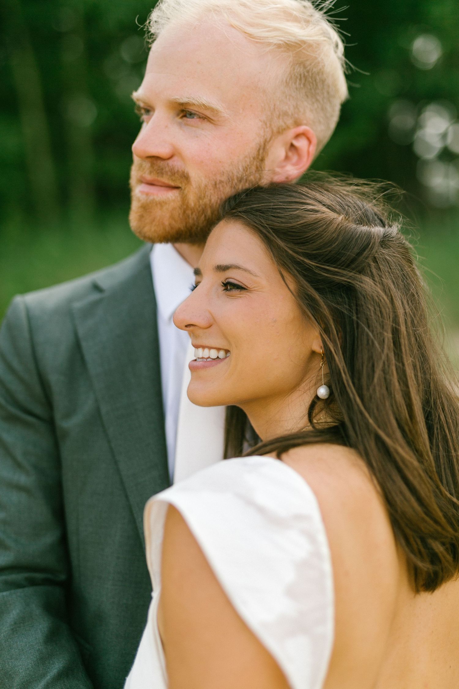 Close up of newlyweds smiling together against a lush green background.