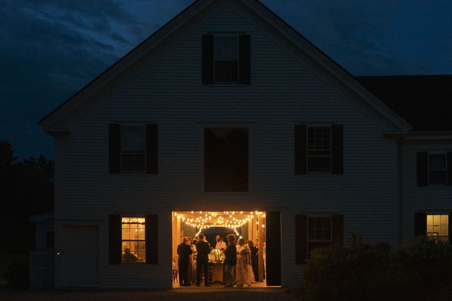 Glowing wedding reception inside the historic 1774 Inn at dusk, guests gathered under string lights in an elegant evening celebration.