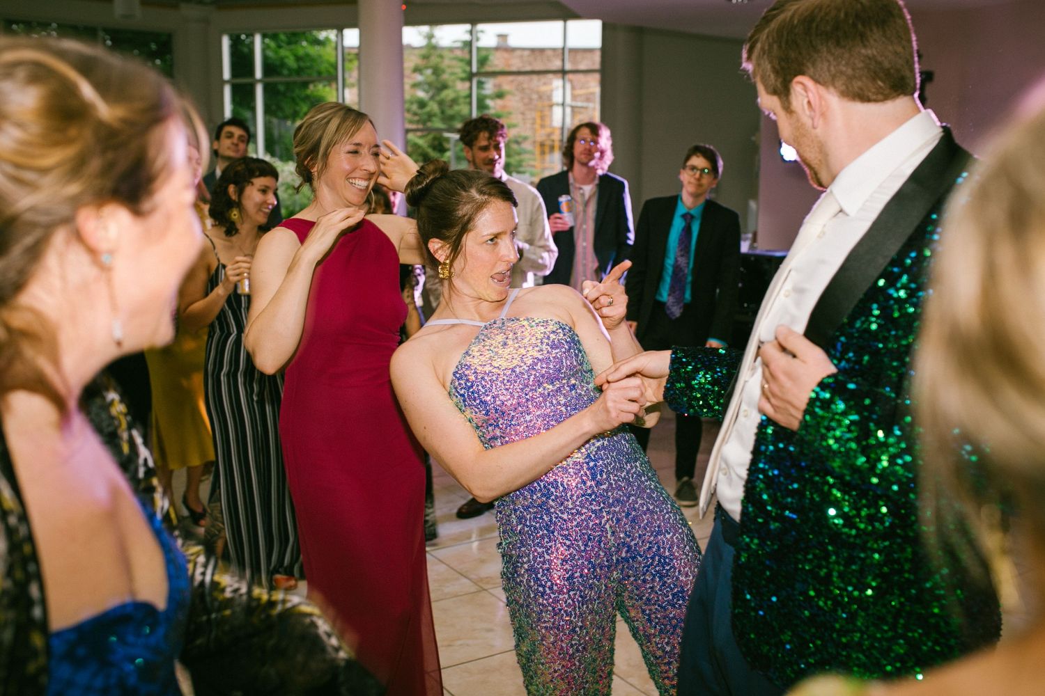 Party guests in formal attire dancing and mingling at an elegant event with people wearing sparkly dresses.