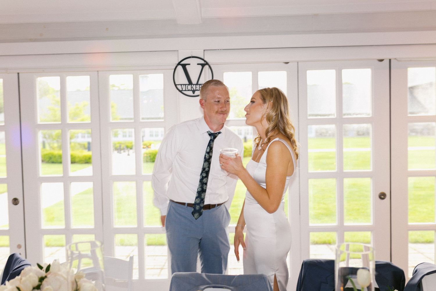 Wedding celebration with elegant table settings and decor under chandeliers in light-filled reception space.