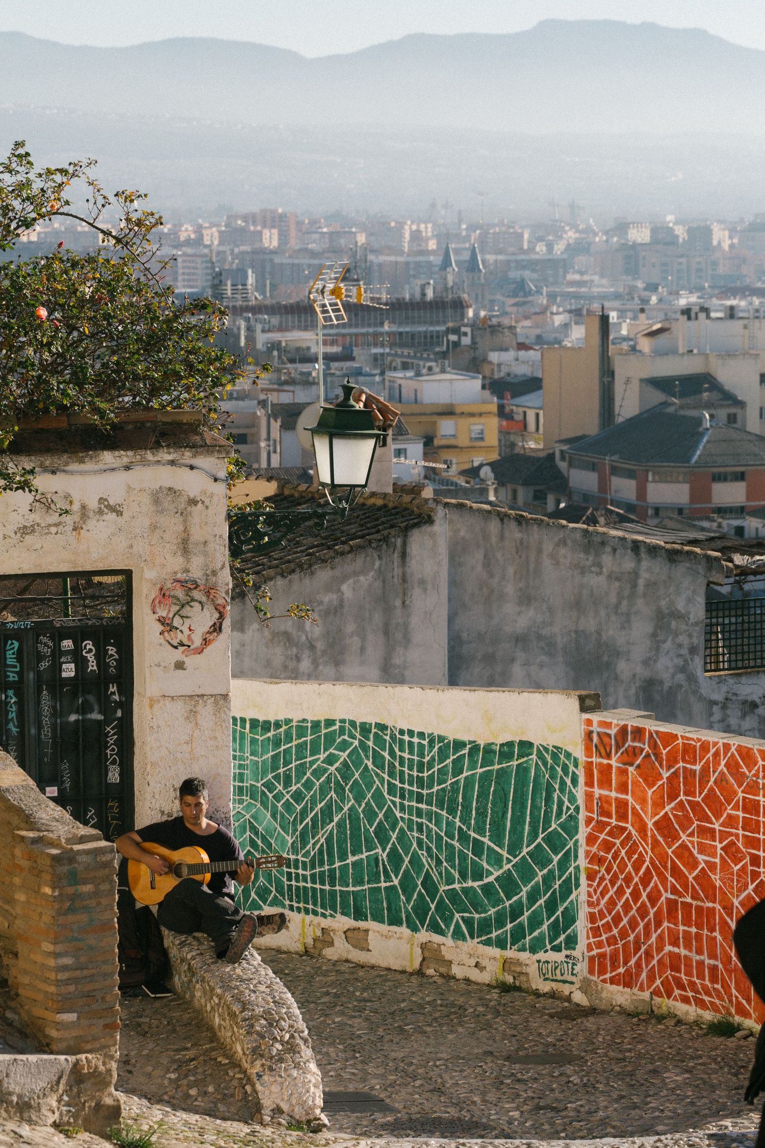 Urban cityscape view with decorative mosaic wall tiles and lantern overlooking misty buildings in the distance.