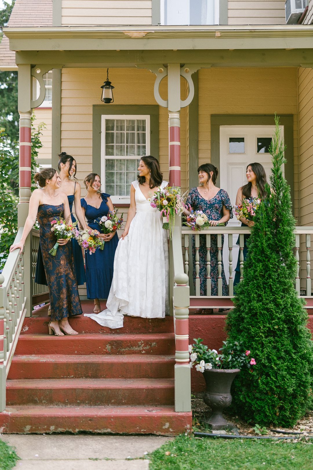 Wedding party gathered on vintage house porch steps with decorative plants.