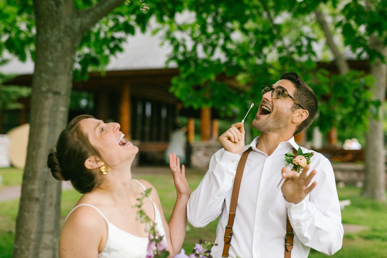 Two wedding guests laugh joyfully together while eating donuts in an outdoor garden setting.