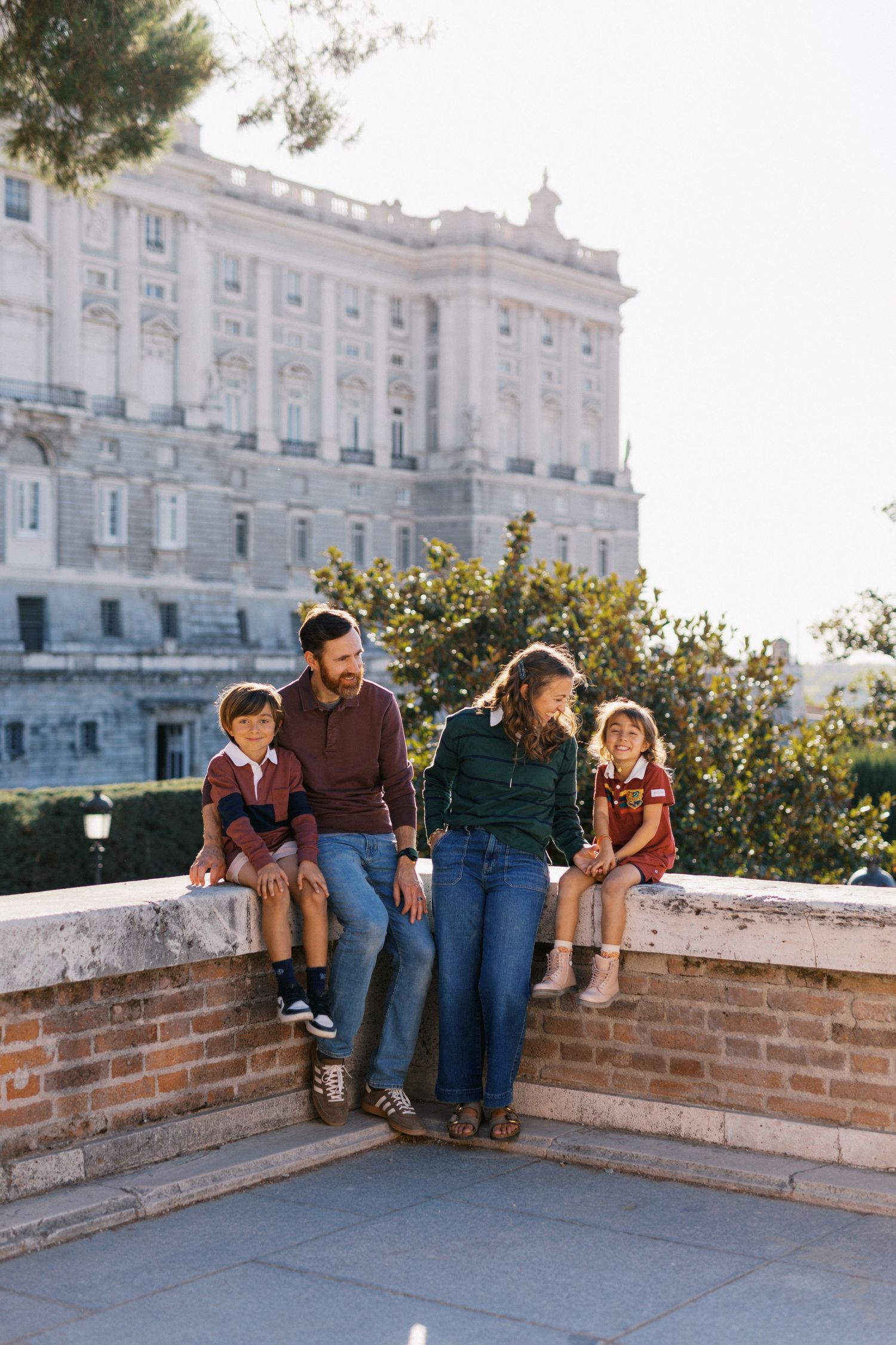 Family of four sitting on a stone wall with a grand palace building in the background.