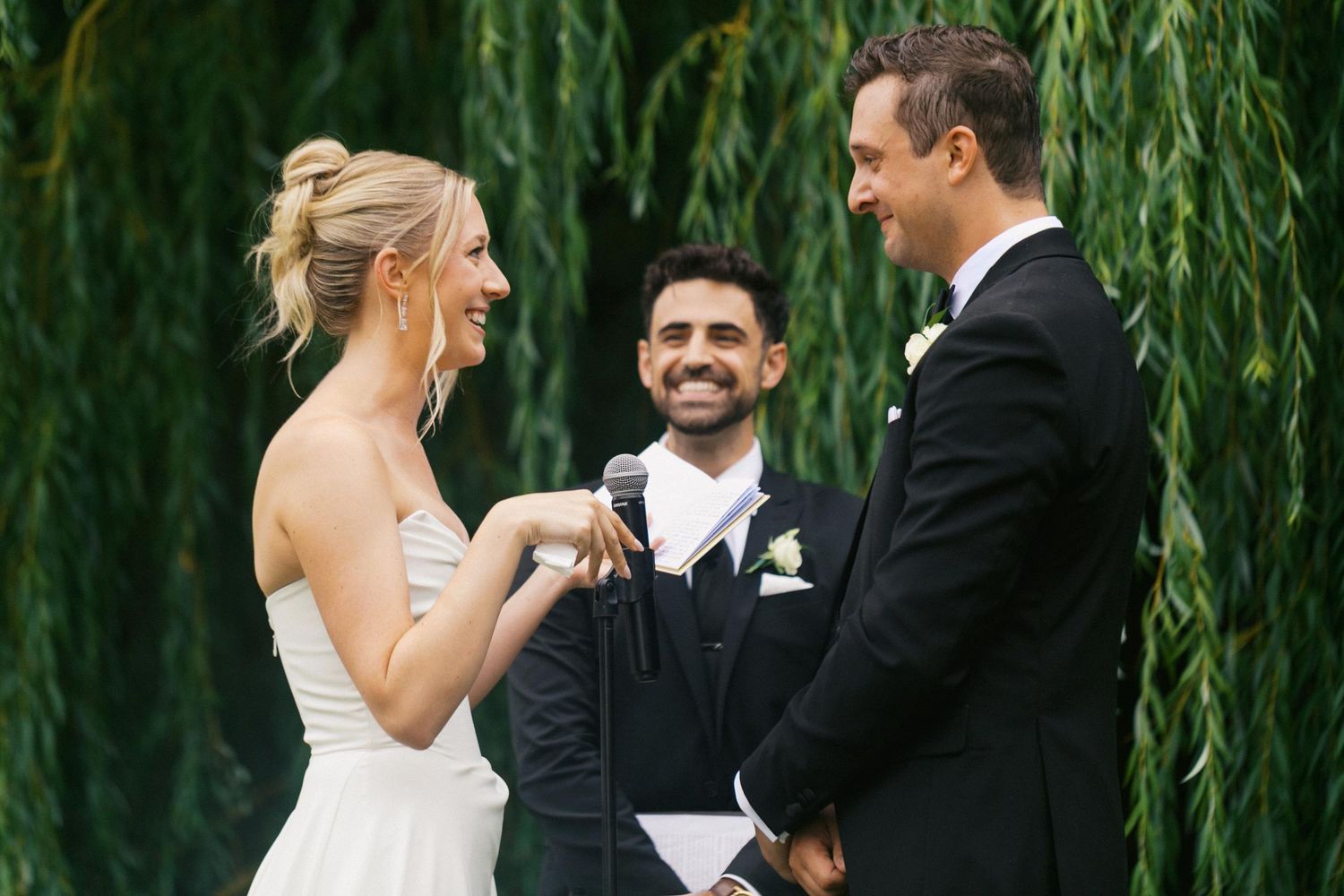 A bride and groom share a joyful moment under a weeping willow tree during their outdoor wedding ceremony at Aurora Cellars in Michigan.