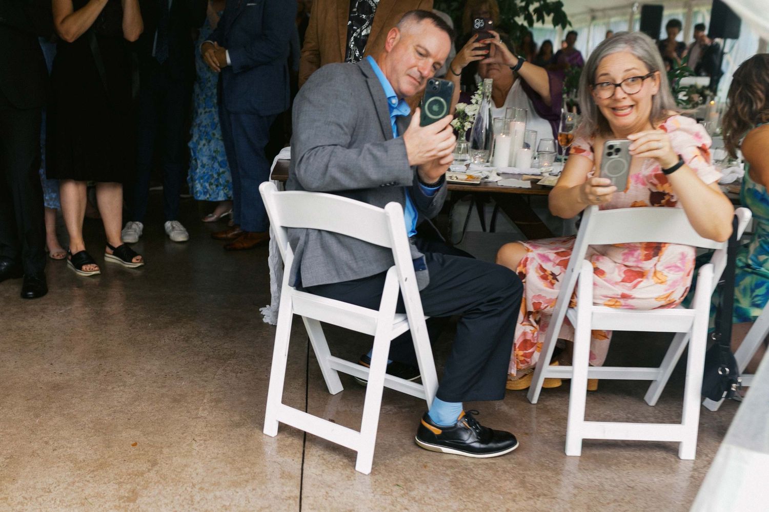 Wedding guests enjoy refreshments and conversation while seated at white folding chairs during an outdoor reception.