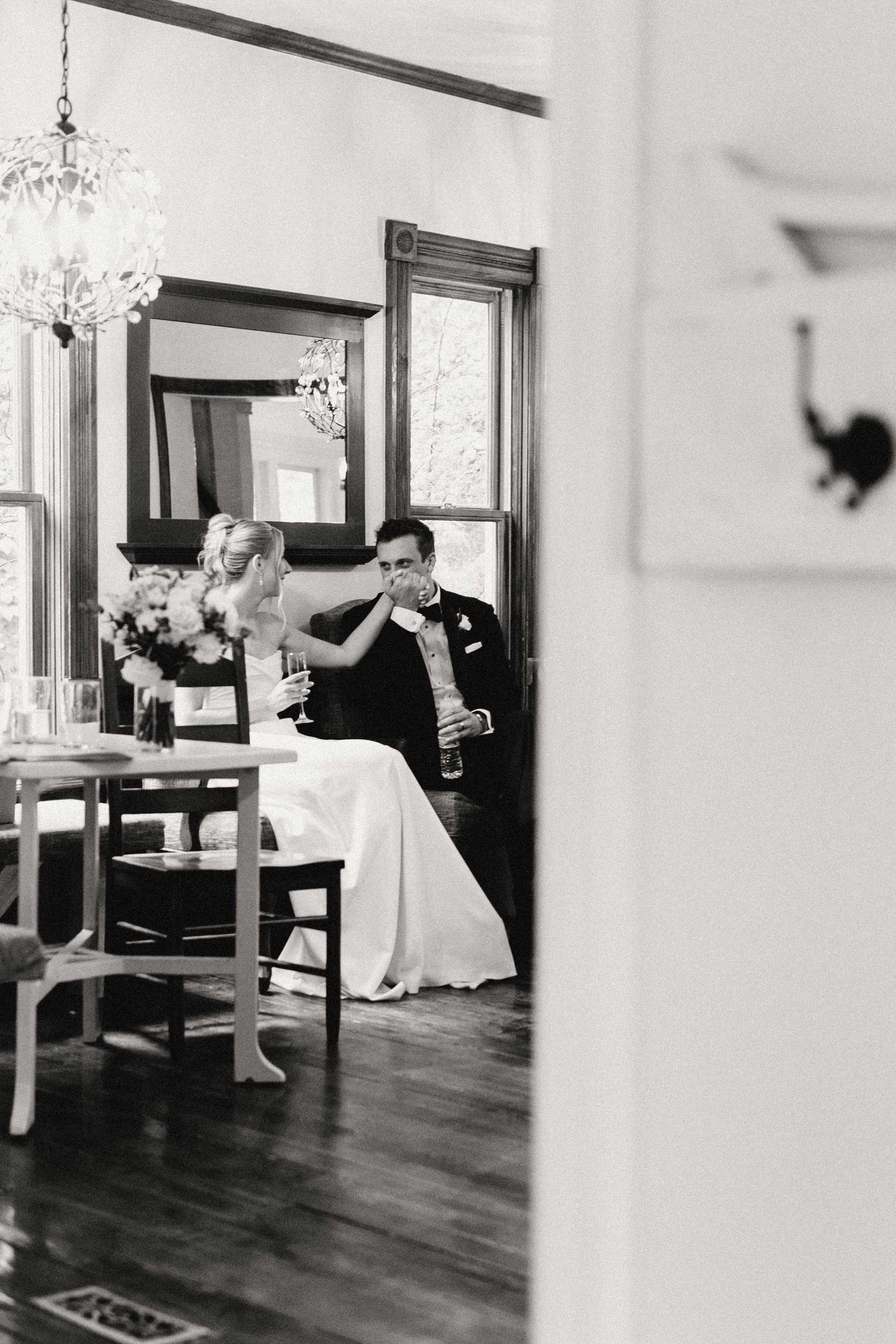Black and white wedding reception photo showing an elegant dining room with chandelier and table settings.