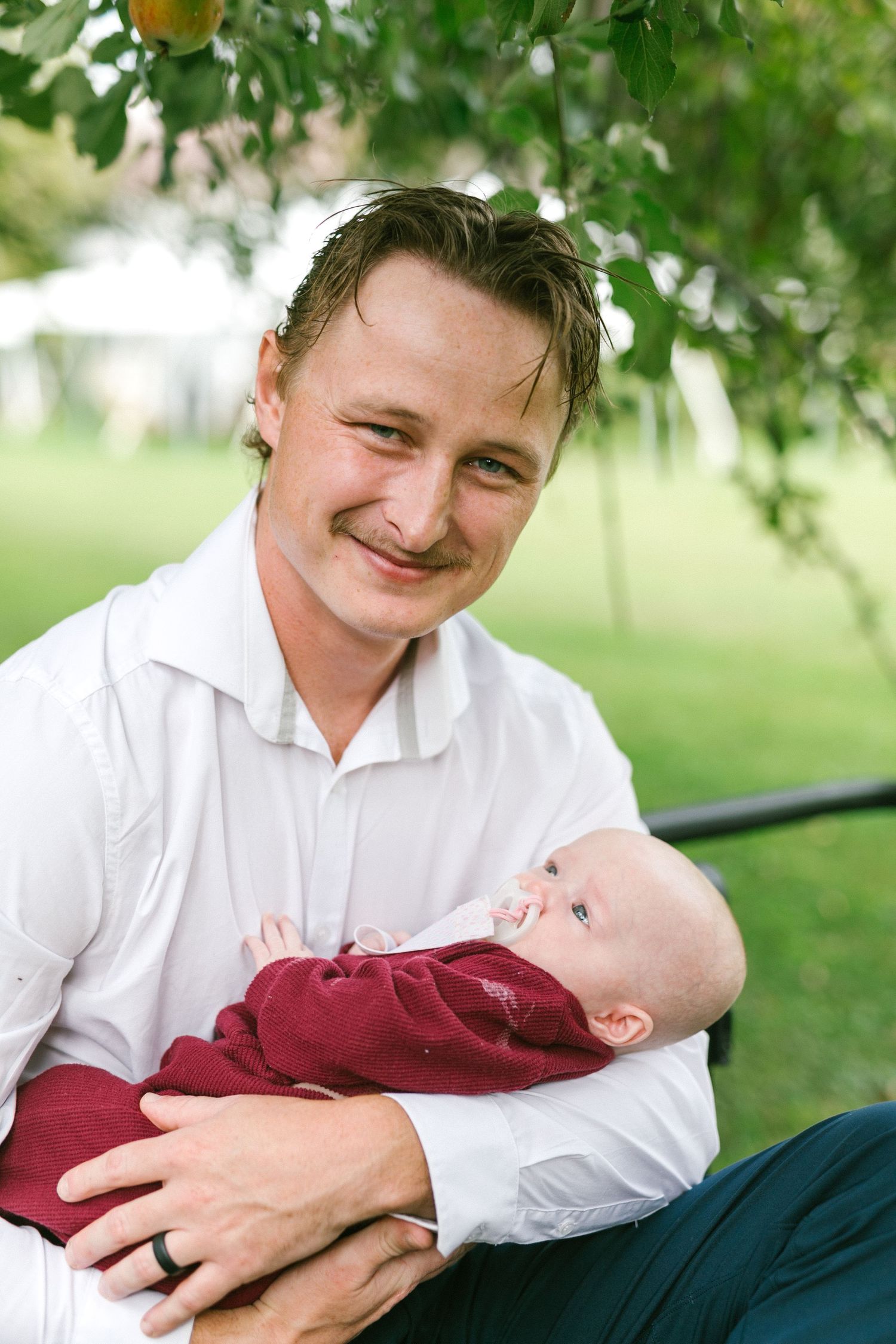 A tender moment between parent and baby under an apple tree in an orchard.