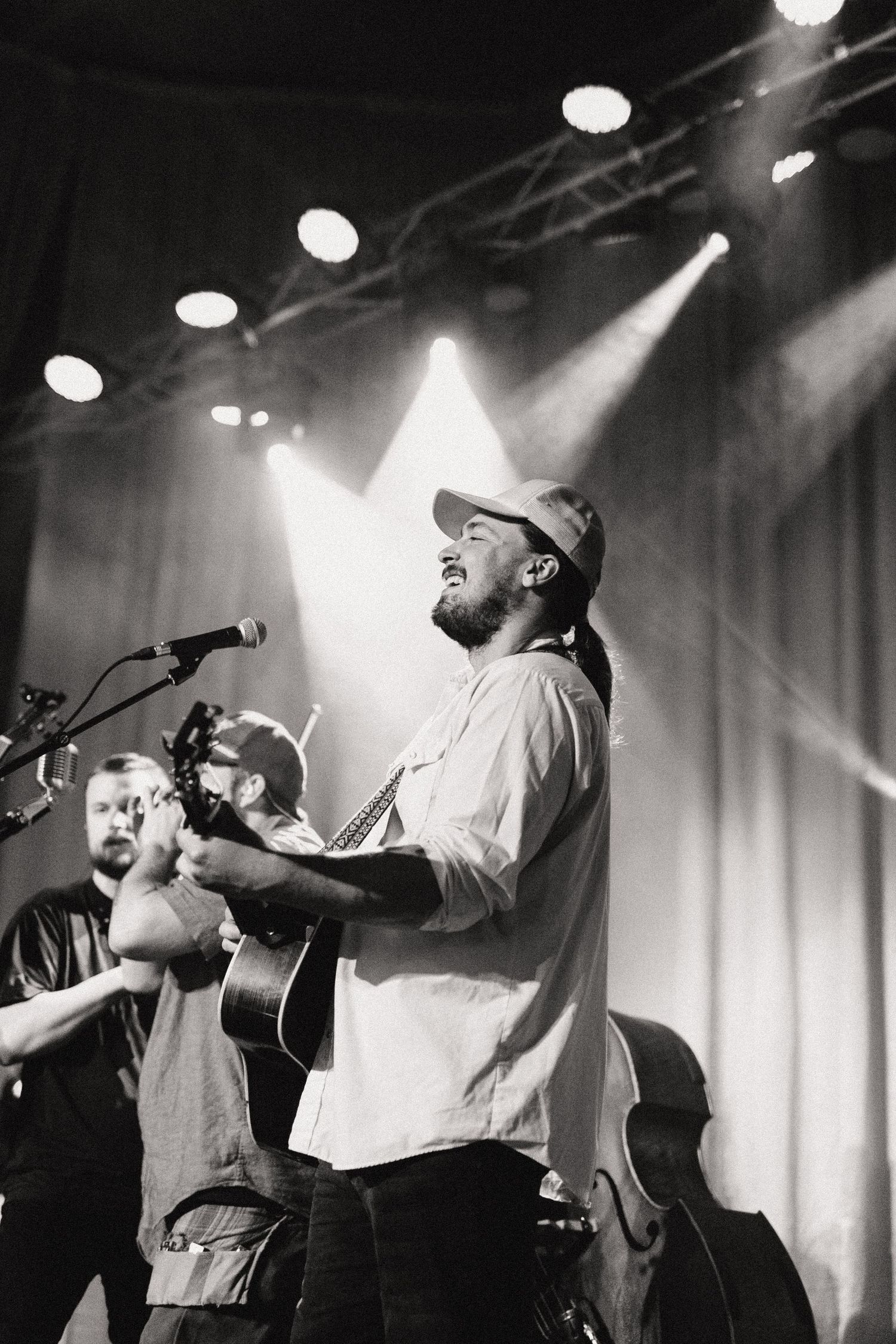A musician performs on stage with an acoustic guitar under dramatic stage lighting at a live concert venue.