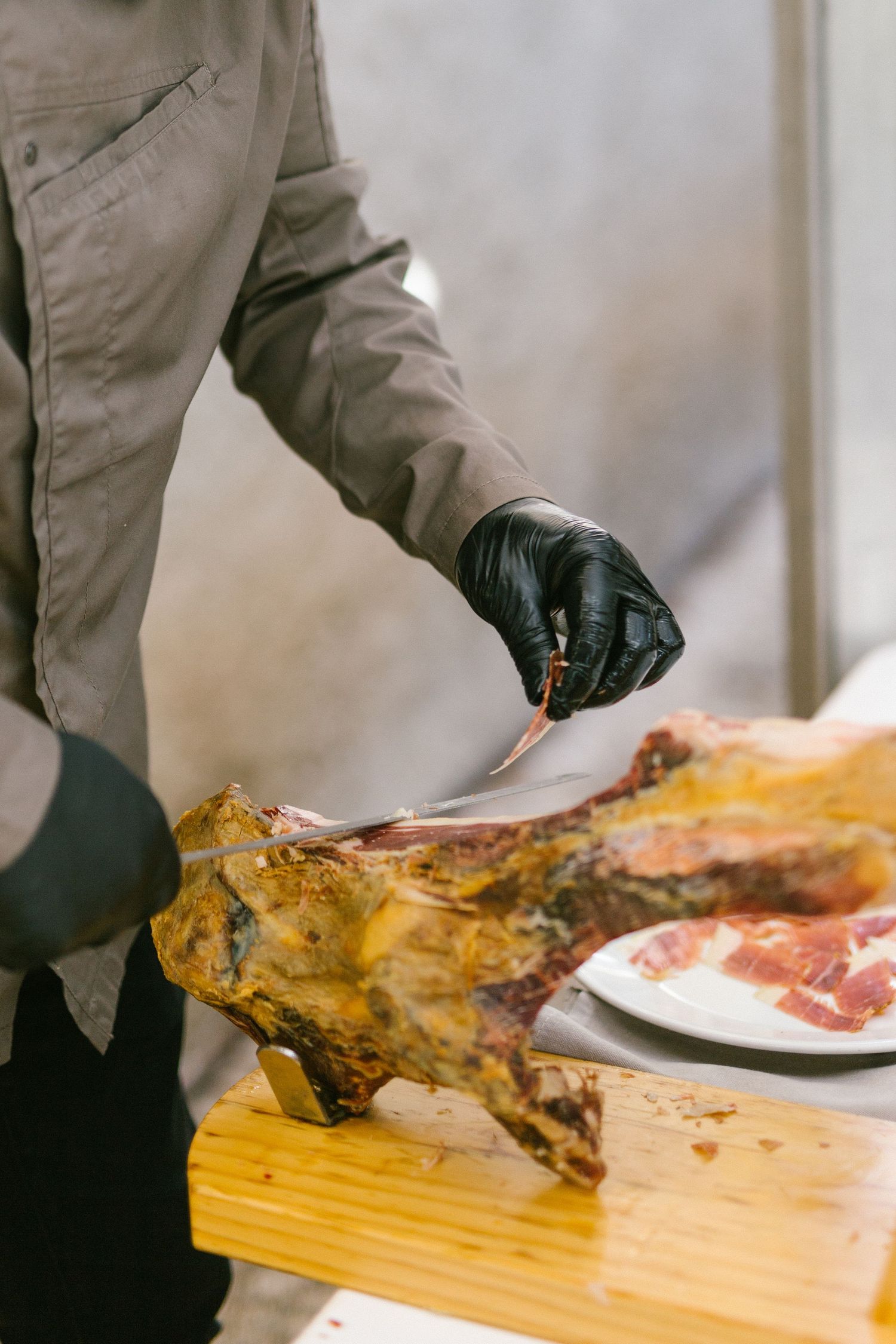Someone wearing black gloves carves meat from a roasted leg at a wooden cutting board.