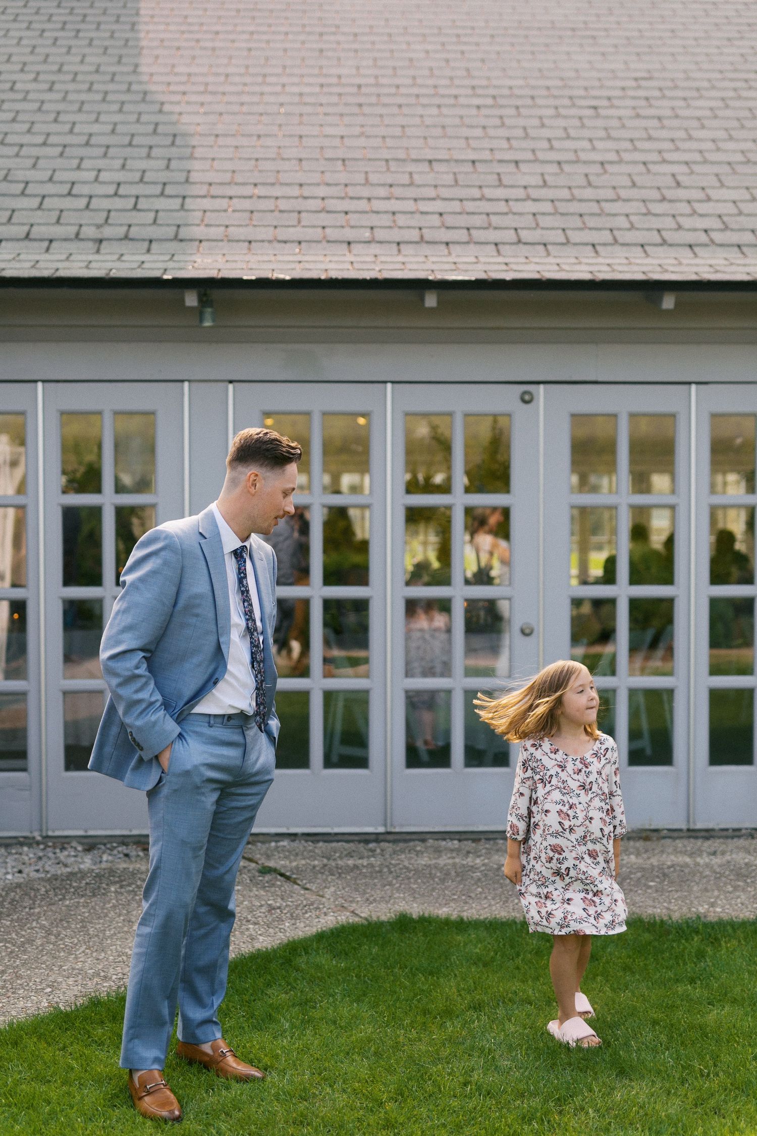 Playful interaction outside white building with grey suit and floral dress.