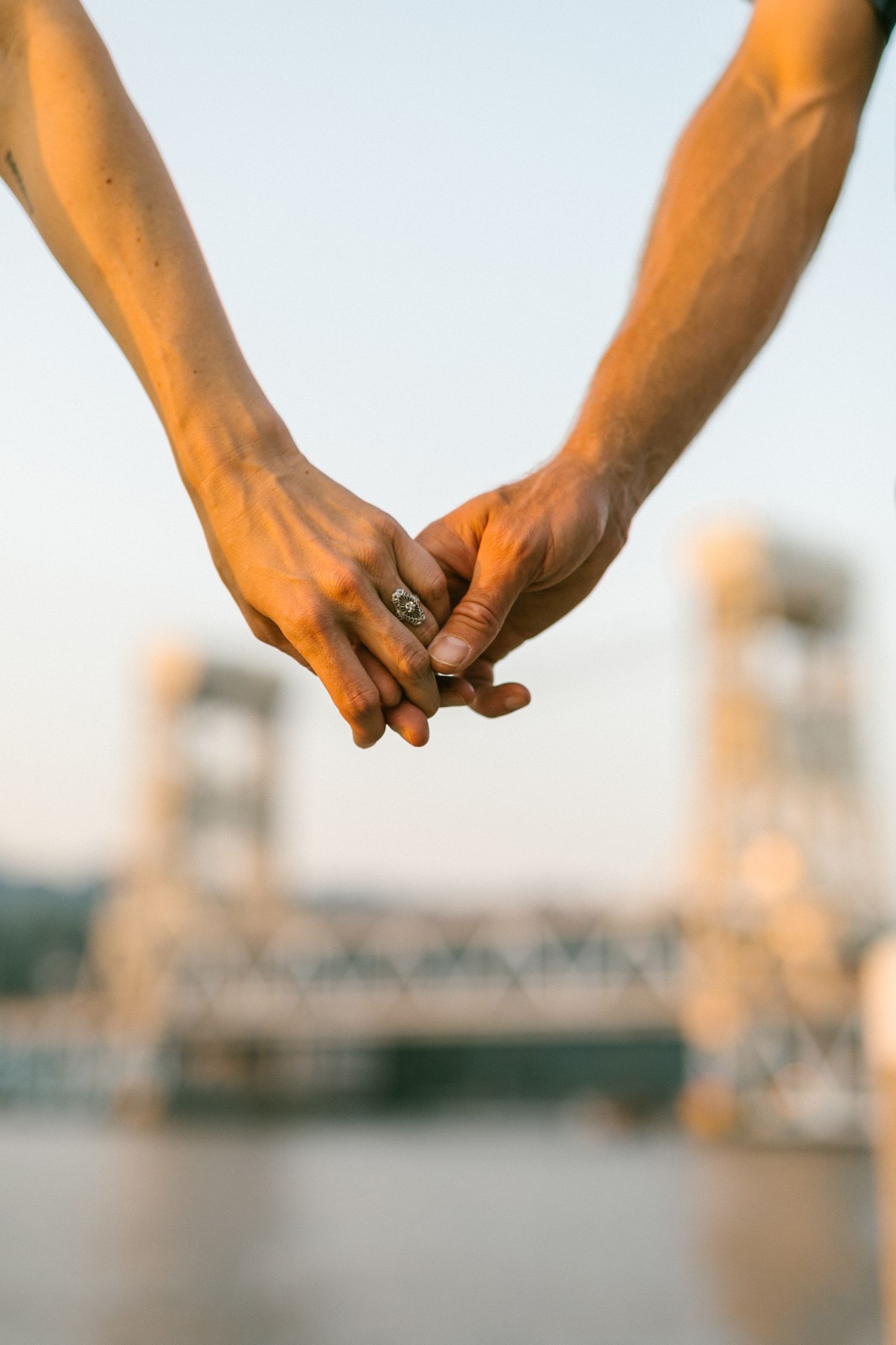 Two hands clasped together against a blurred architectural background in warm sunset lighting.