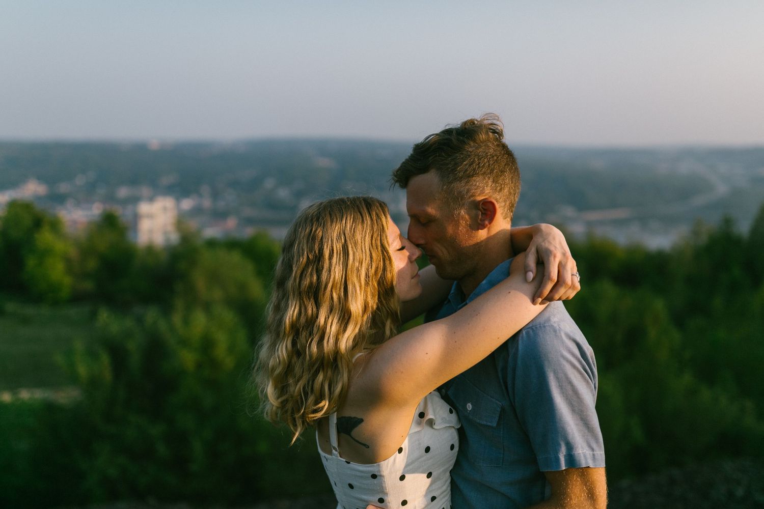A romantic moment between a couple in summer attire against a scenic hilltop backdrop.