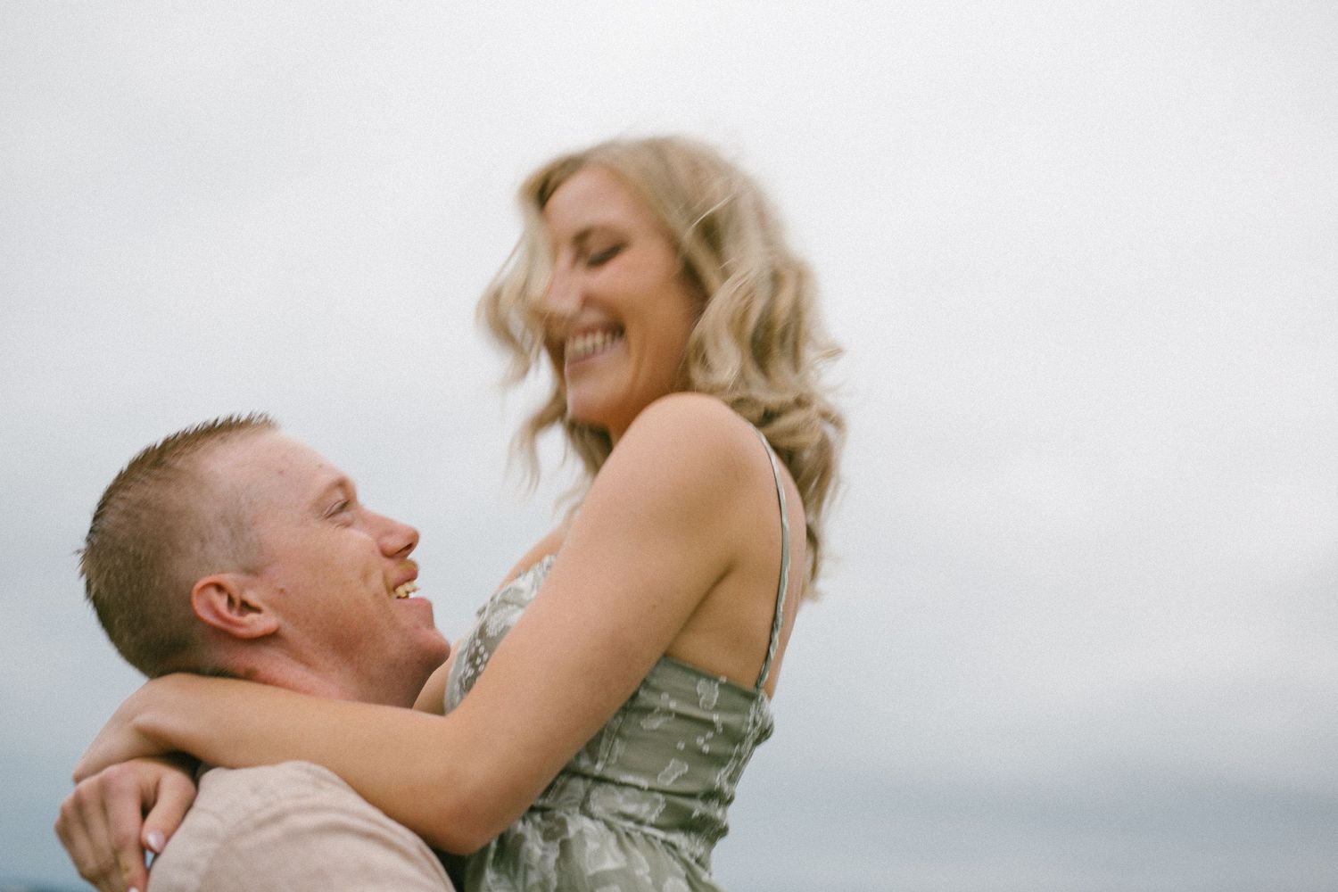 Couple shares joyful moment together against cloudy sky backdrop.