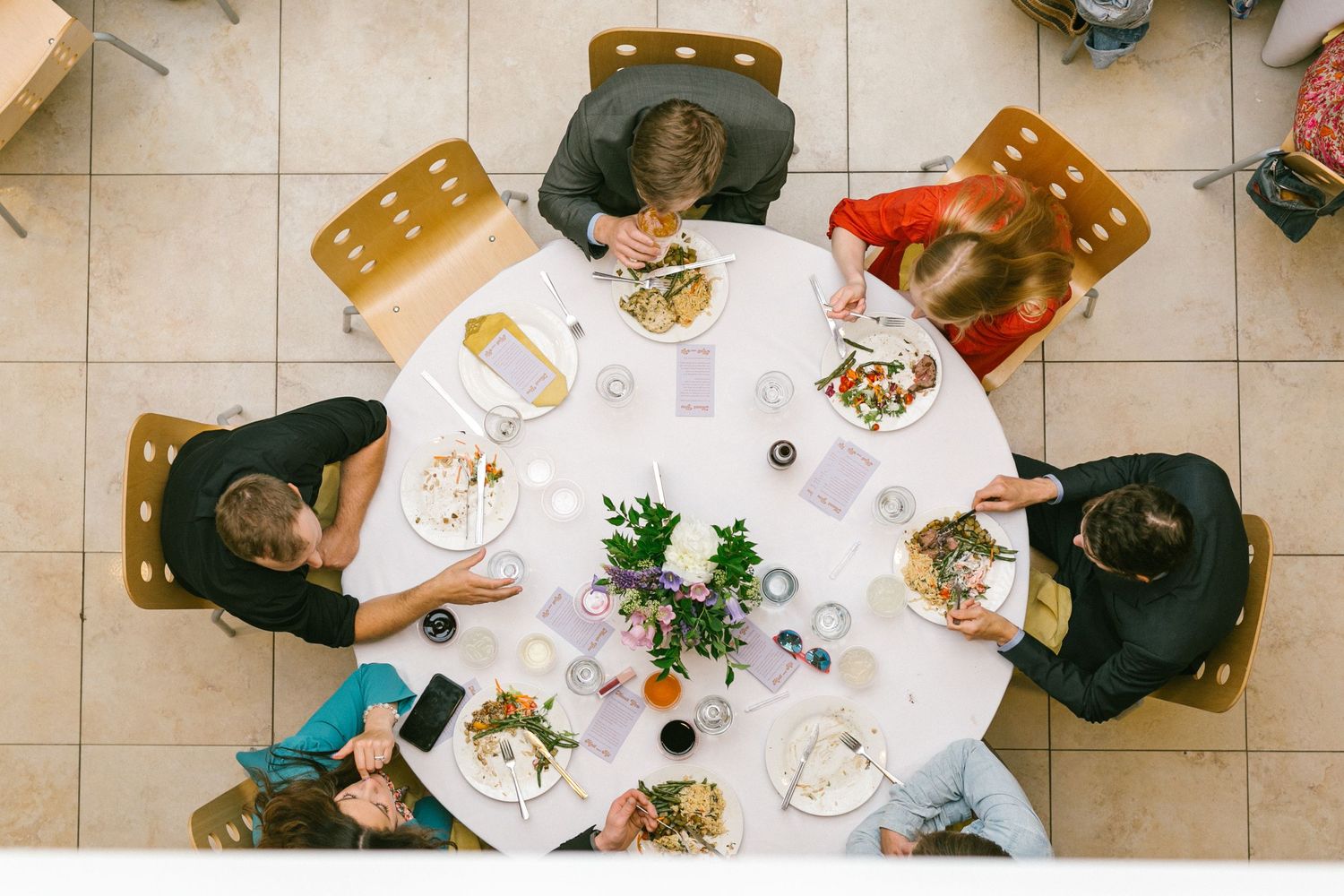 Overhead view of a round dining table with guests seated around plates of food and centerpiece.