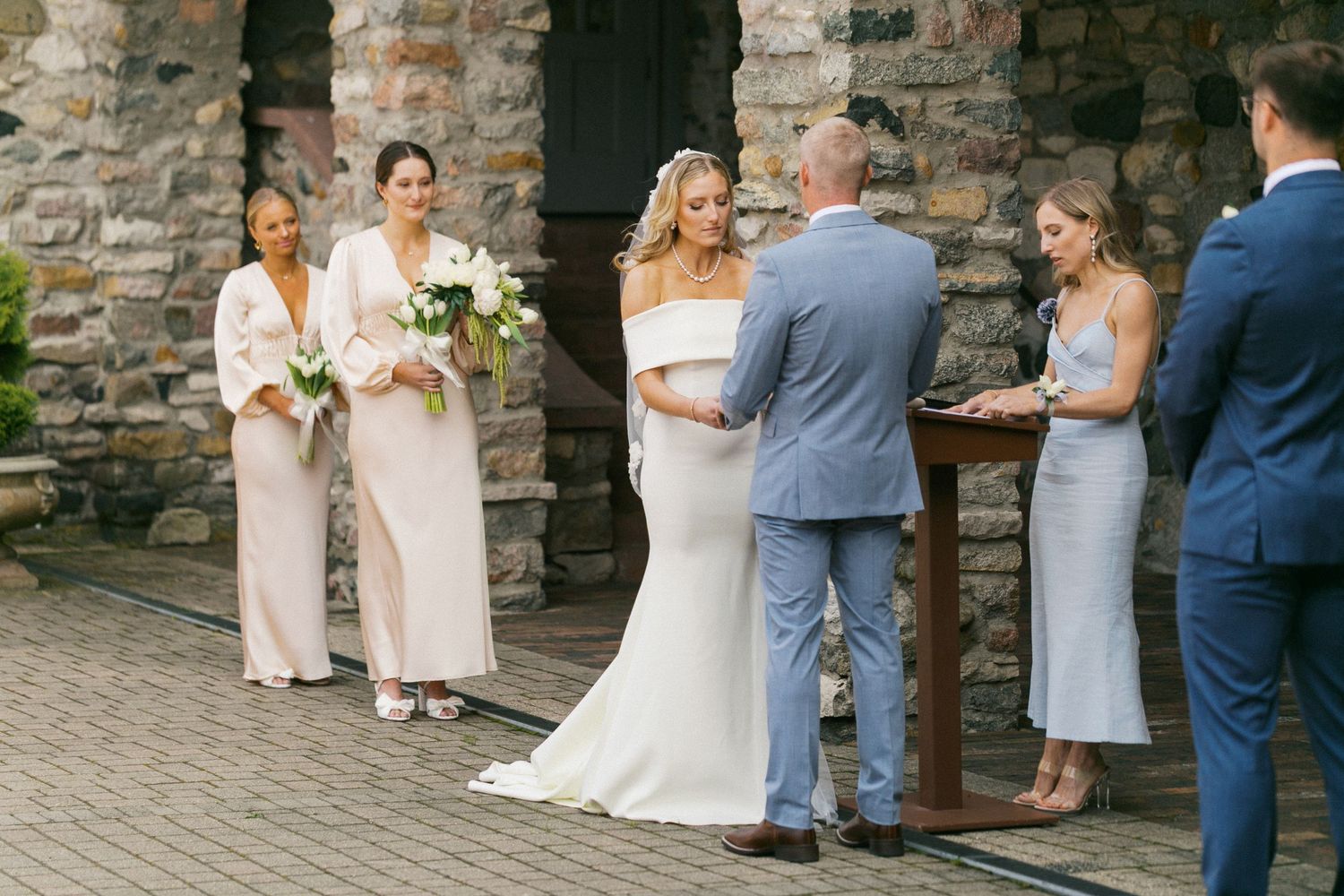 Wedding party posing against rustic stone wall at outdoor venue.