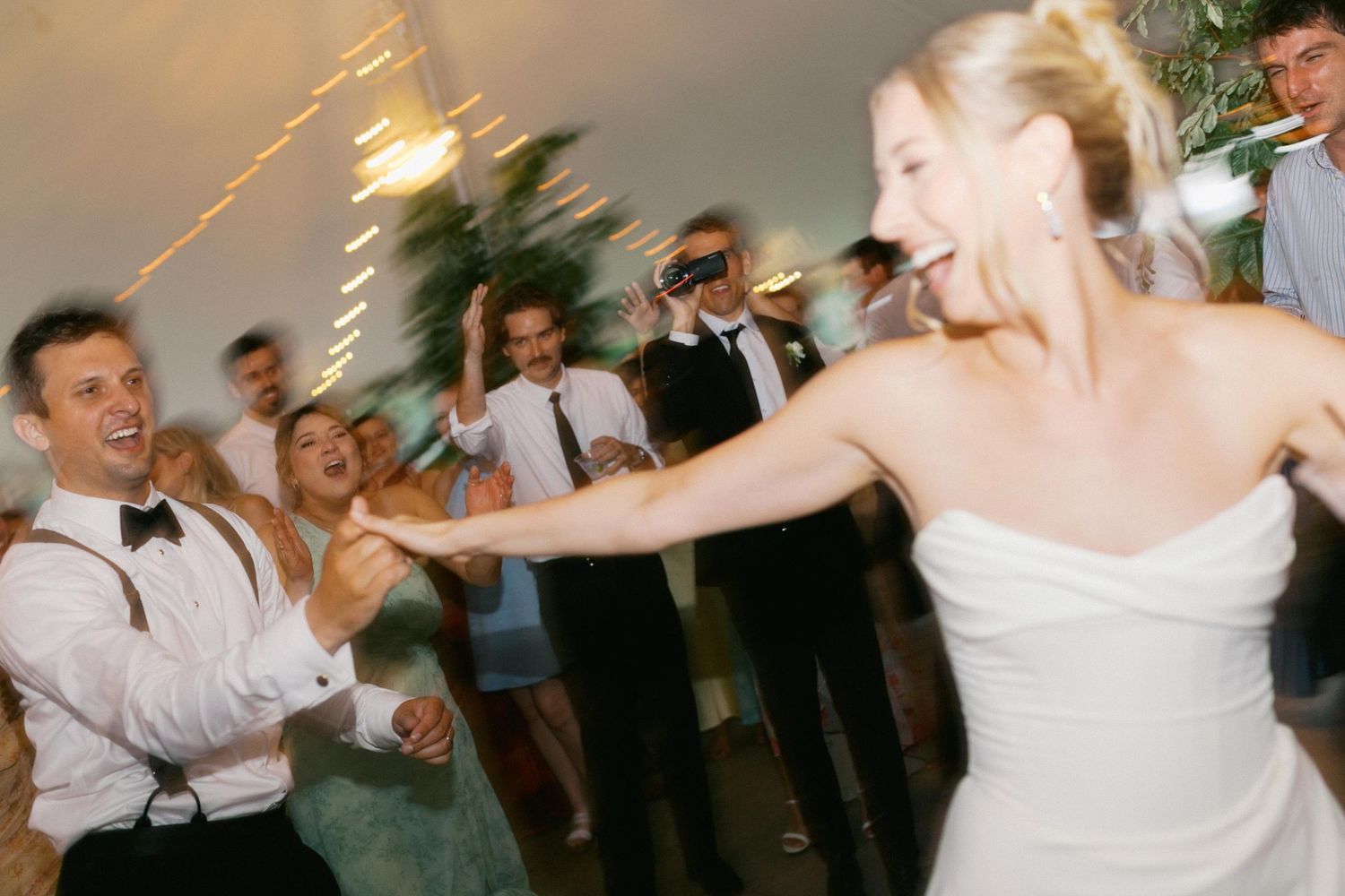 Wedding guests and the bride and groom dance and celebrate together on a lively dance floor during an evening reception celebration.