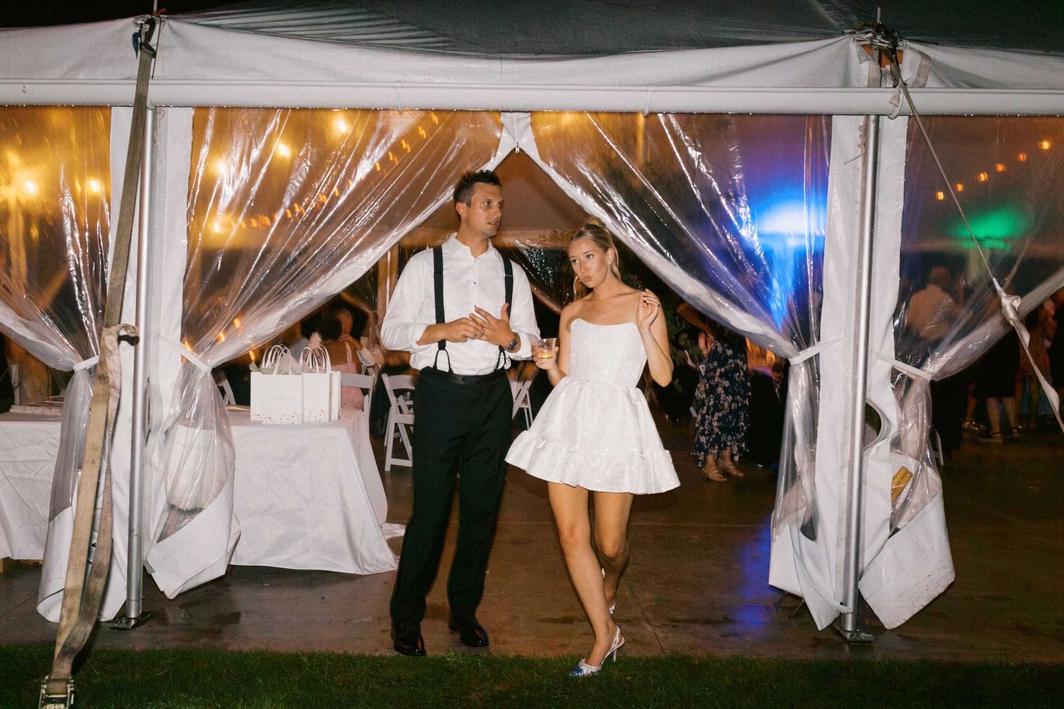 A couple dances under an elegant white tent with string lights at an outdoor evening reception.