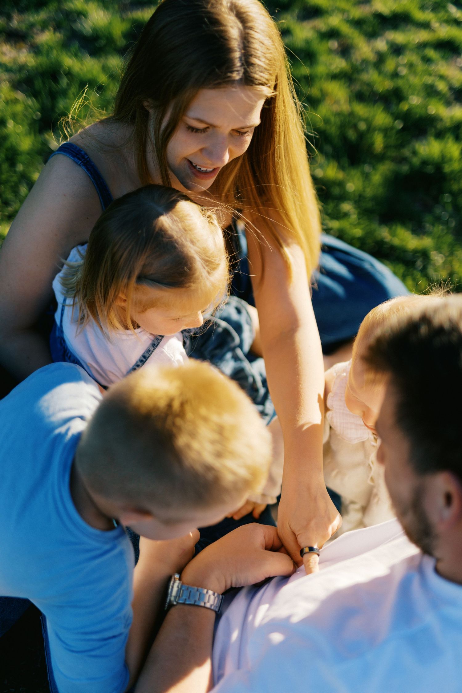Loving mother smiling while holding children close together on green grass outdoors.