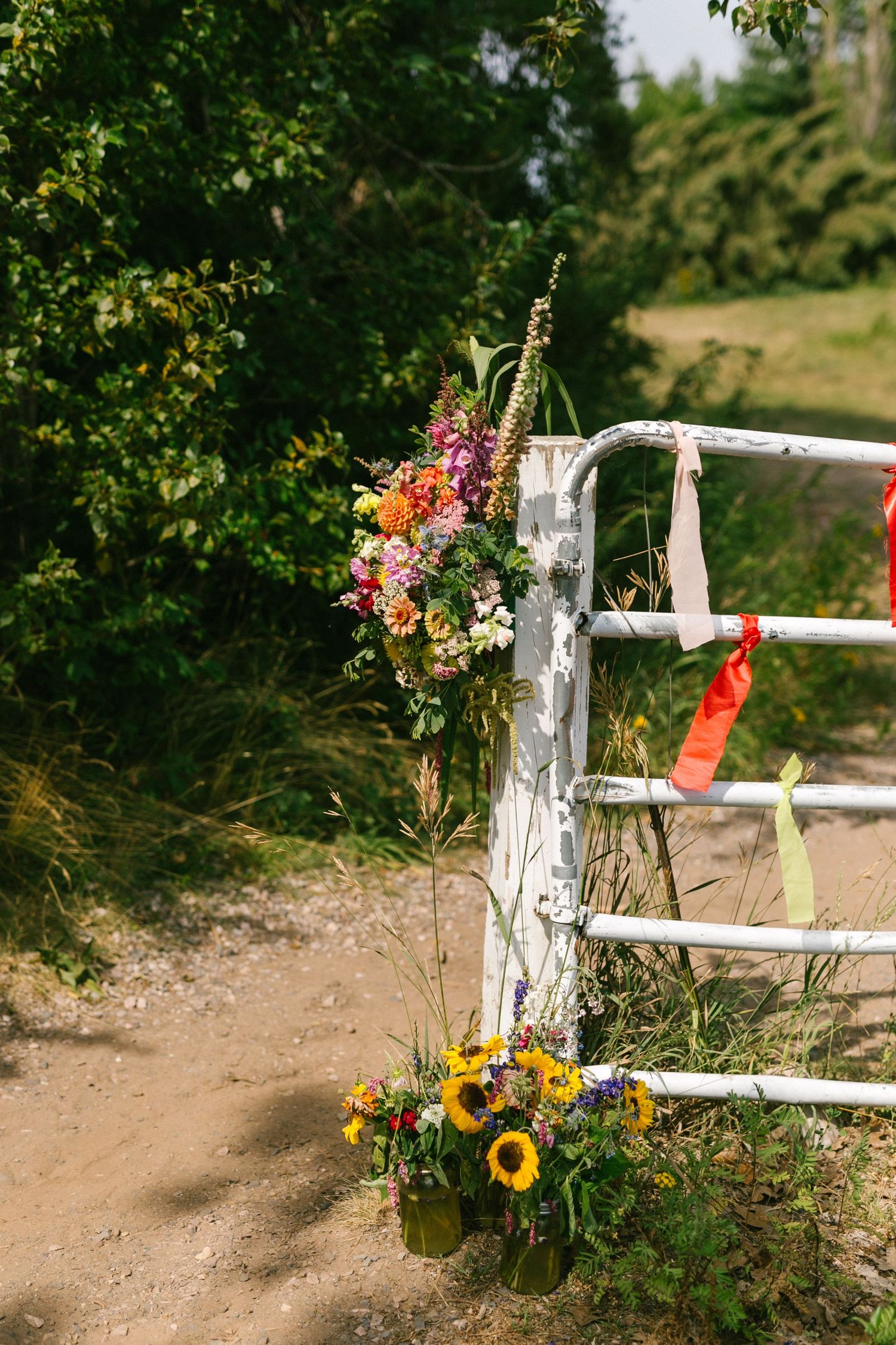 Rustic white fence post decorated with colorful wildflowers and sunflowers along a dirt path in a garden setting.