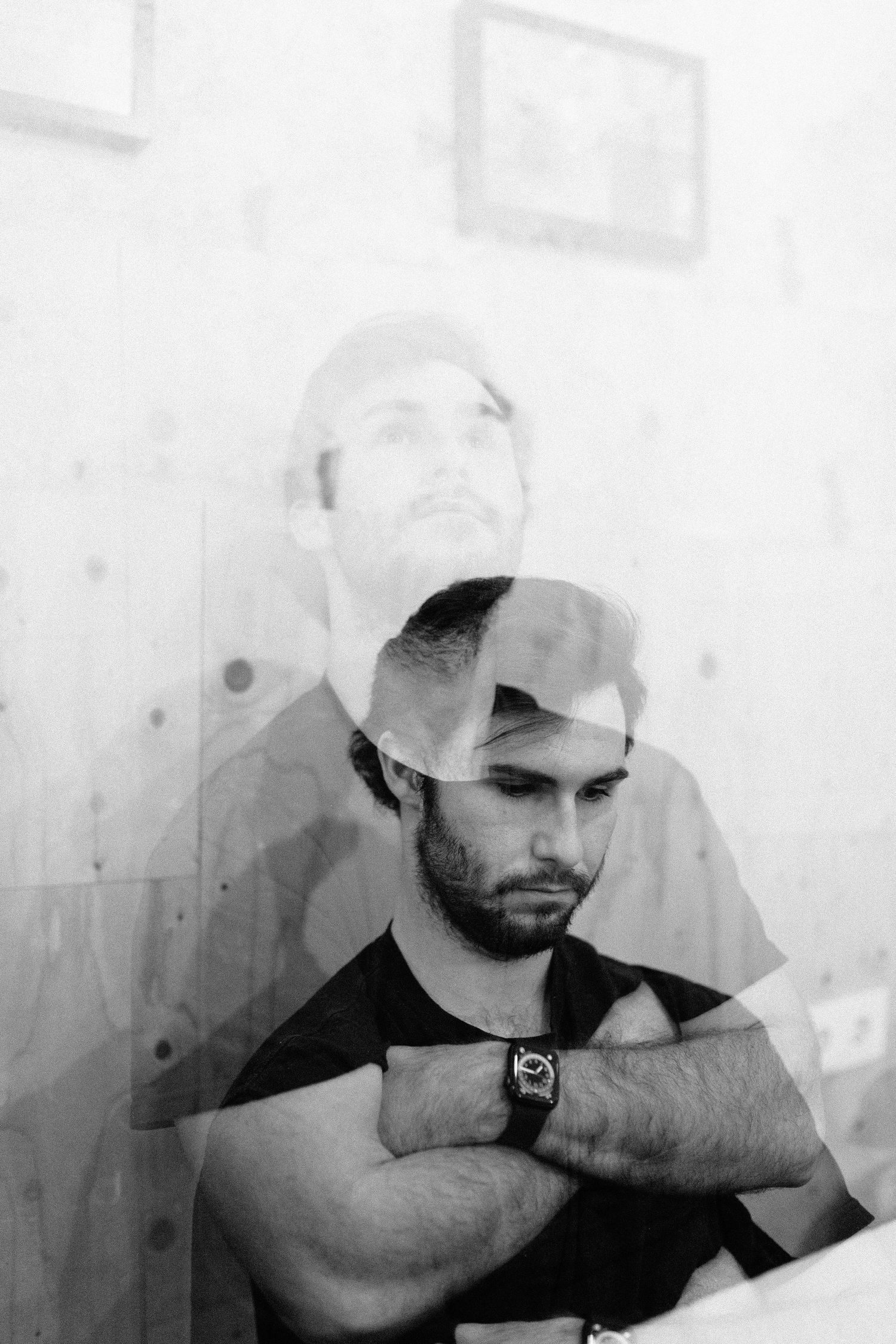 Black and white double exposure portrait of a bearded man with arms crossed.