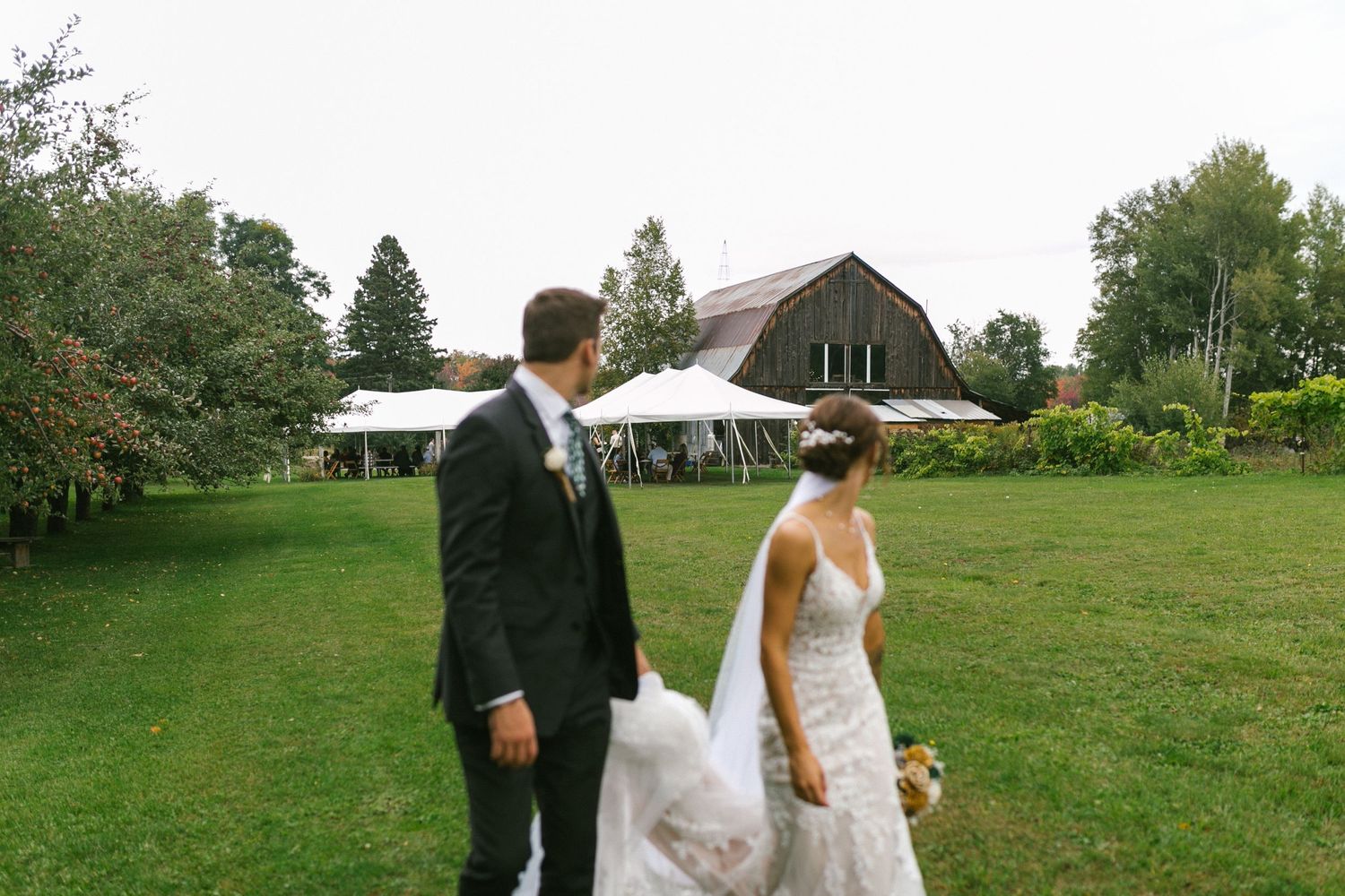 A couple walks together on a lush green lawn during an outdoor wedding celebration.