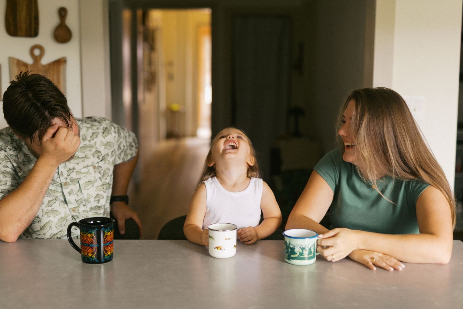 Candid family moment of parents and laughing toddler sharing joy together at a kitchen table.