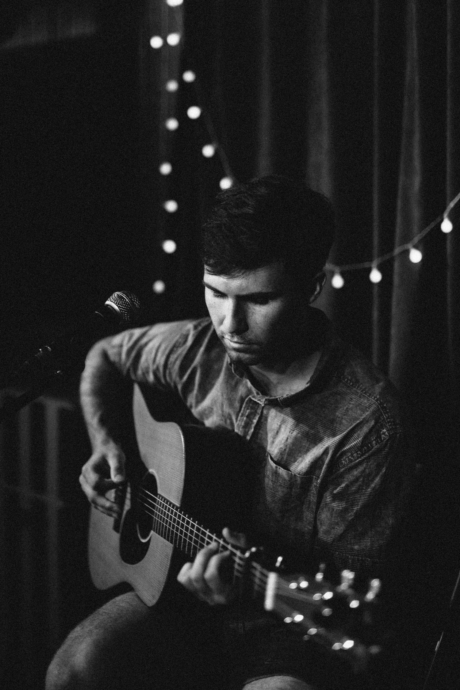 Black and white photo of a man playing acoustic guitar on stage with bokeh lights.