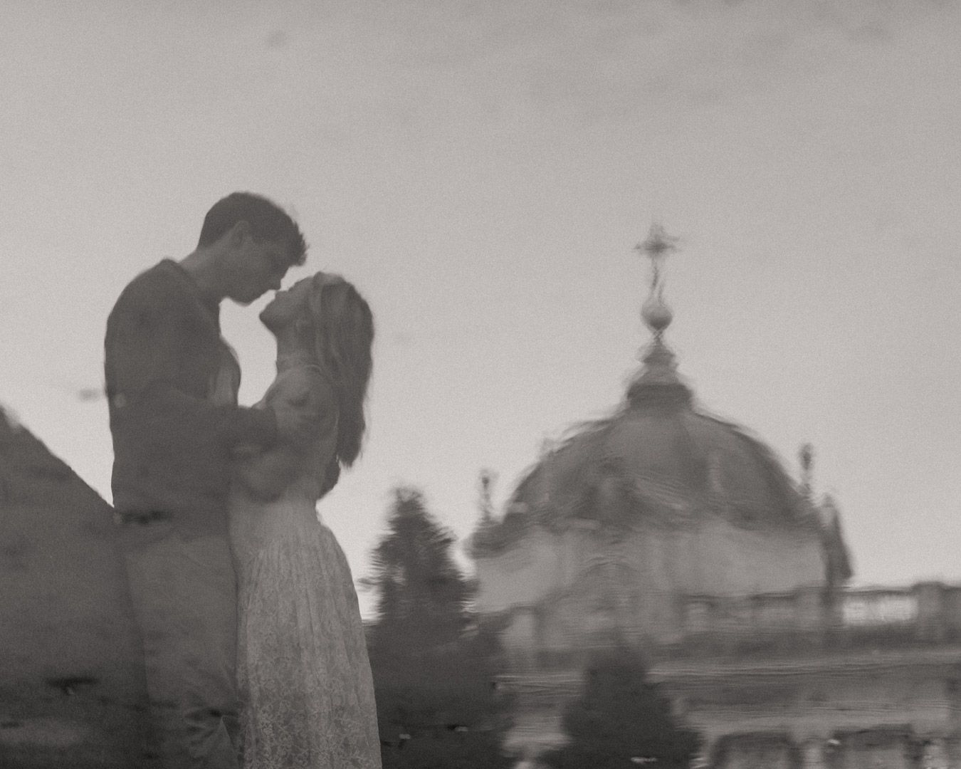 Romantic black and white reflection of couple embracing near domed cathedral.