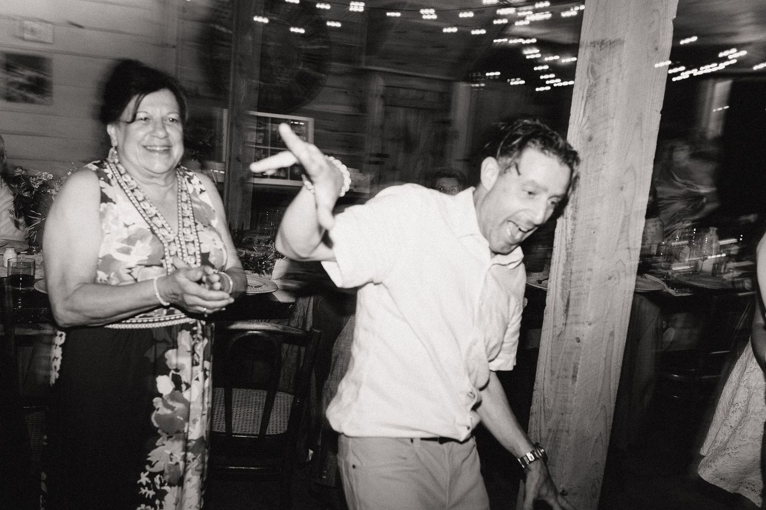 Black and white photo of a man and woman dancing and laughing at an intimate wedding reception.
