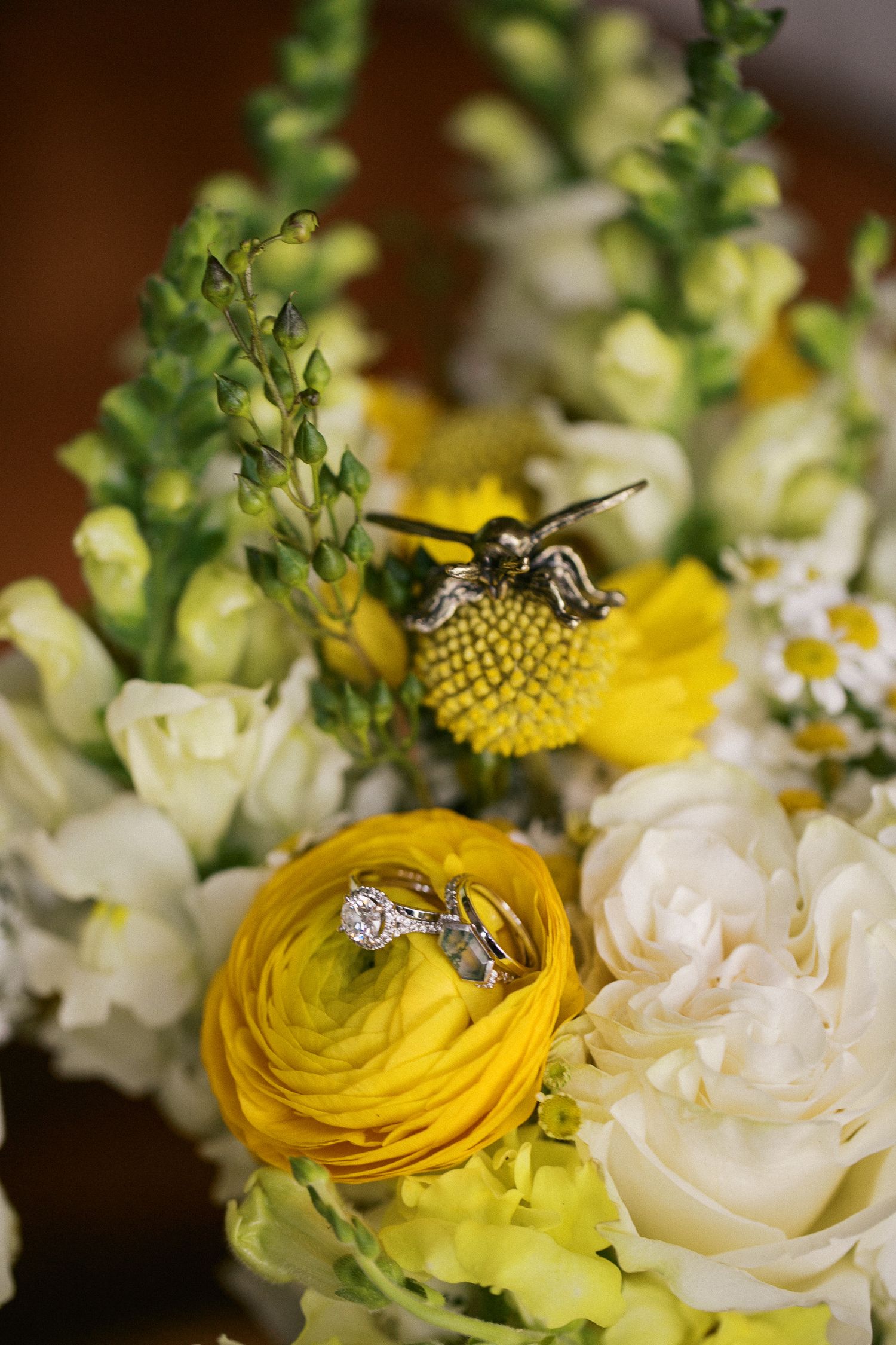 Wedding rings resting on yellow ranunculus flowers in a bridal bouquet with white roses and snapdragons.