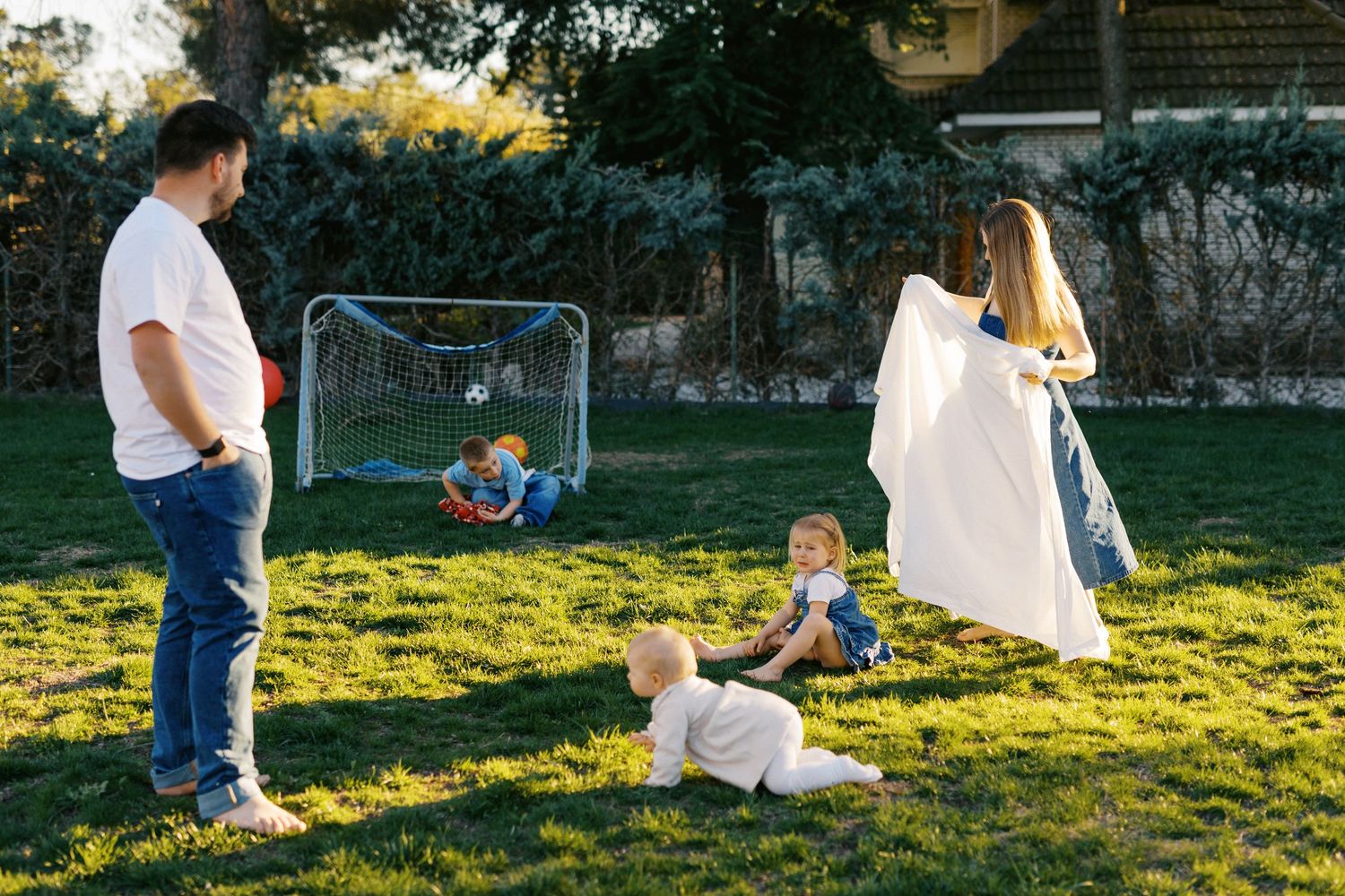 Happy family playing together on green lawn with soccer goal in sunny backyard.