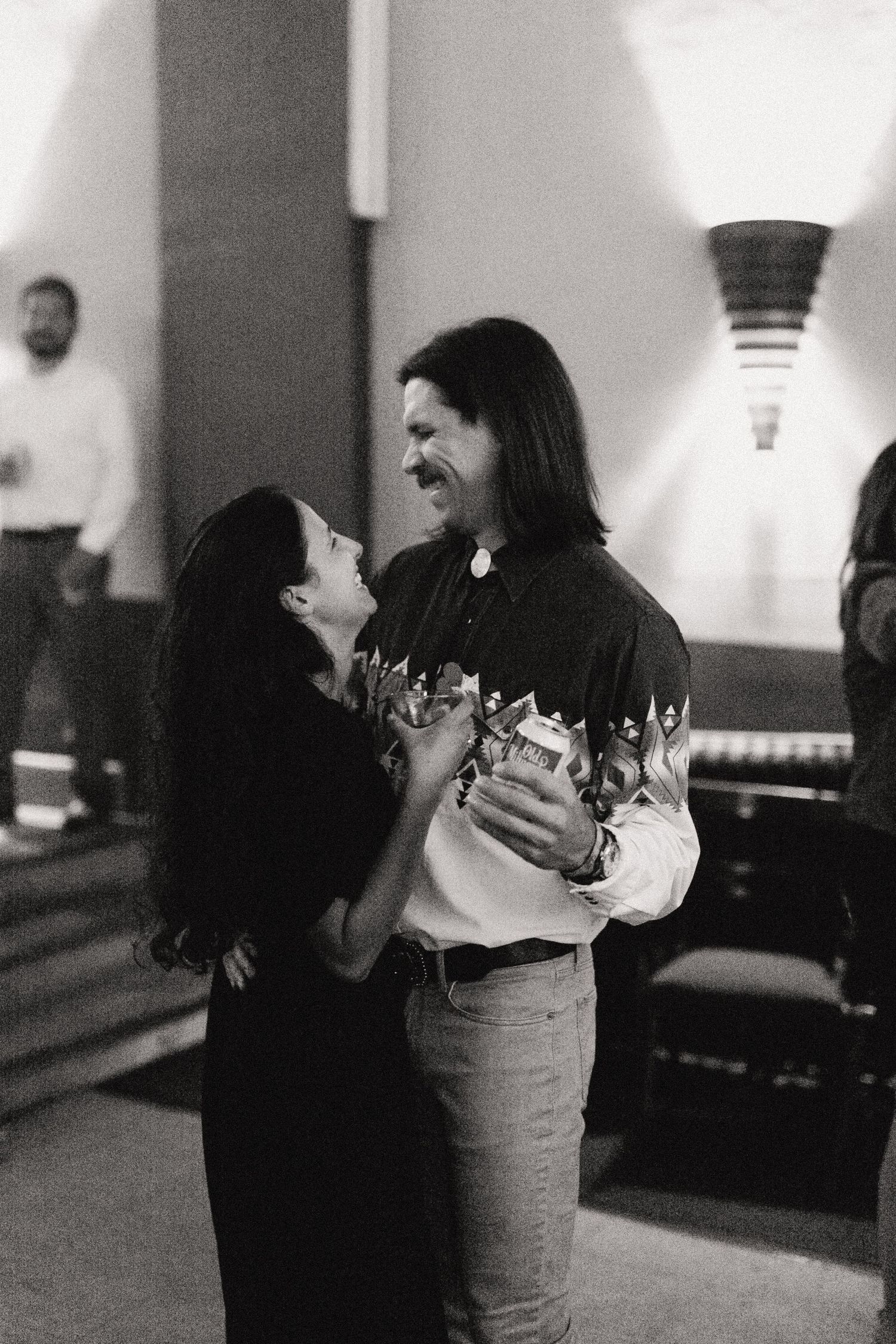 A black and white candid photo of a dancing couple sharing a joyful moment together in an indoor setting.