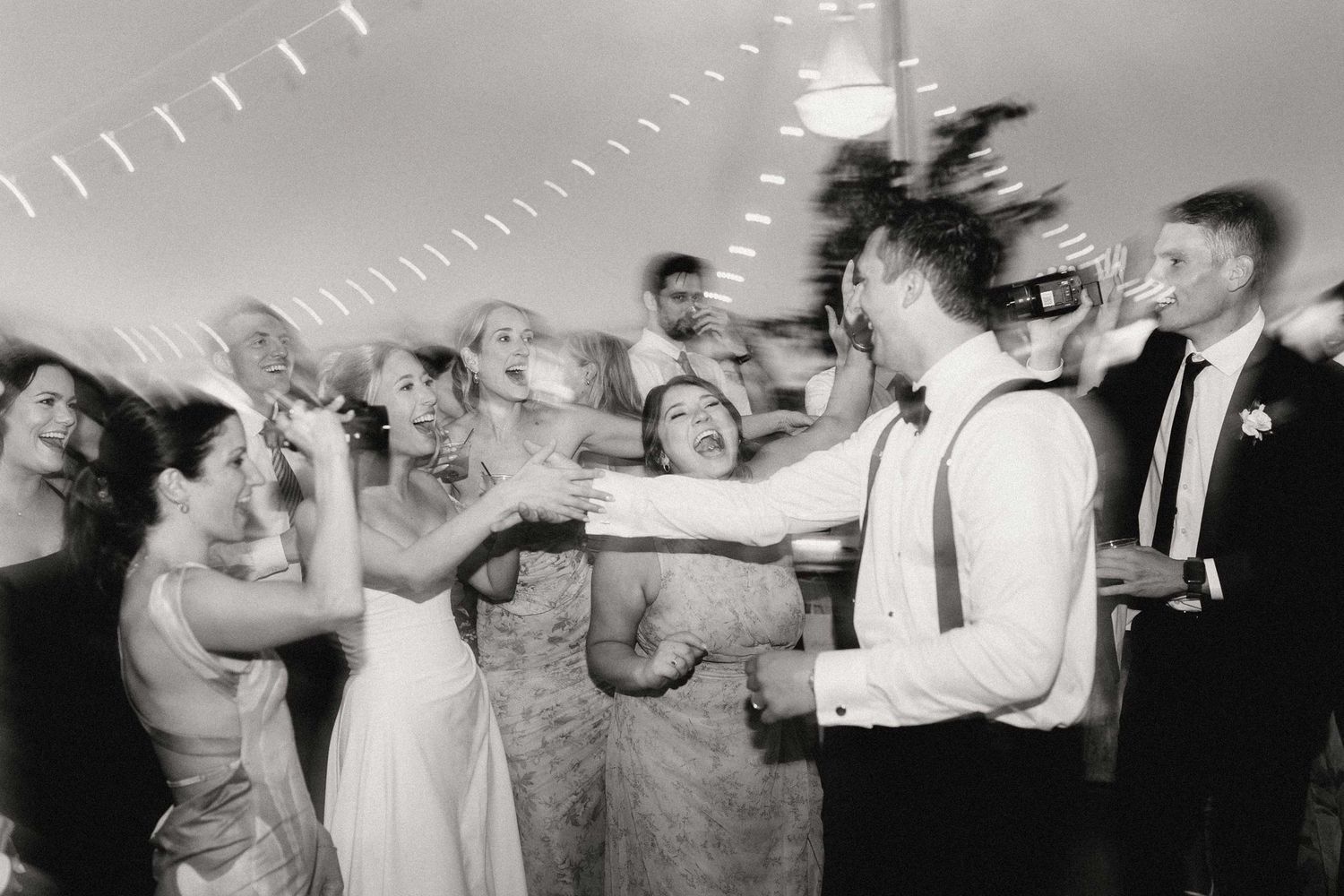 A sequence of black and white photos showing wedding guests dancing and celebrating at a reception party.