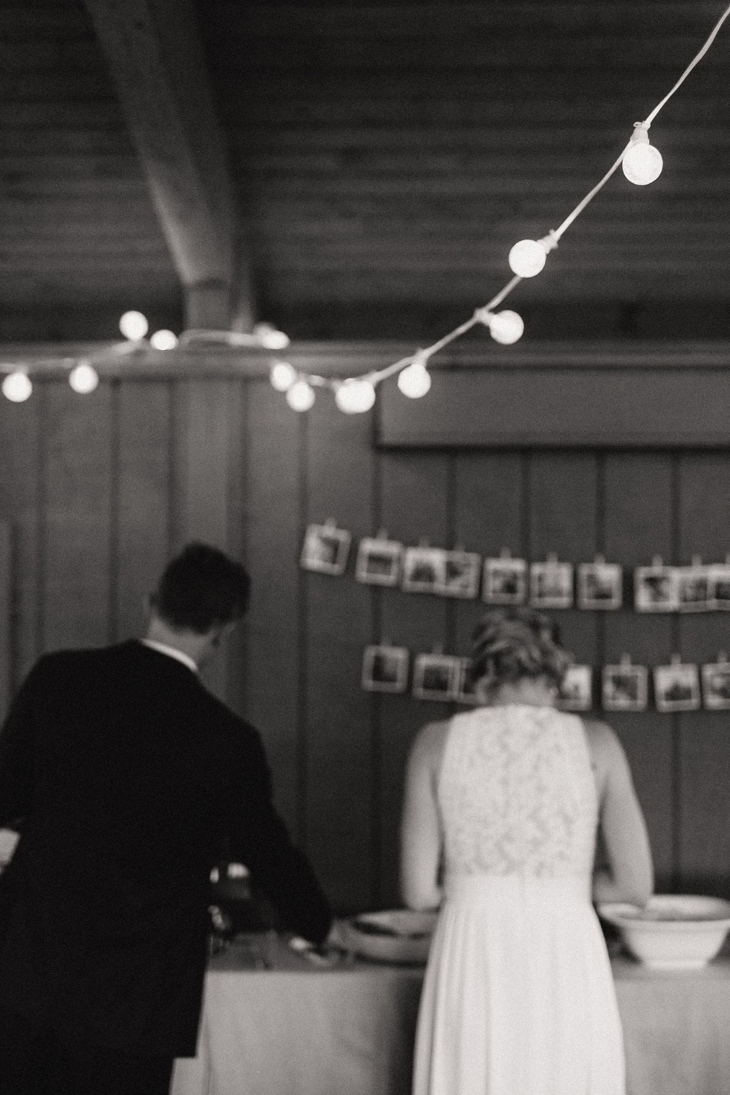 String lights and hanging photos decorate a rustic wooden wall at an indoor event.